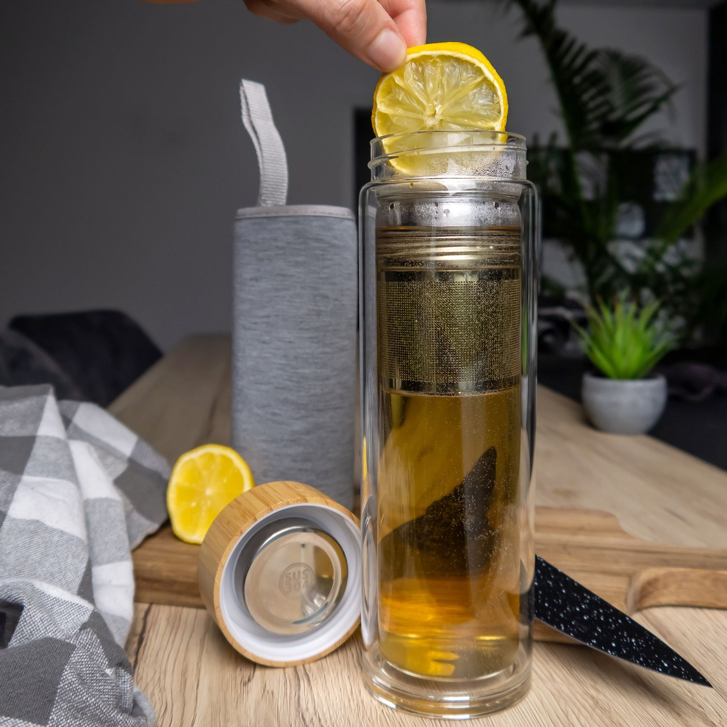 Eine Person gibt eine Zitronenscheibe in einen Glas-Tee-Infuser.