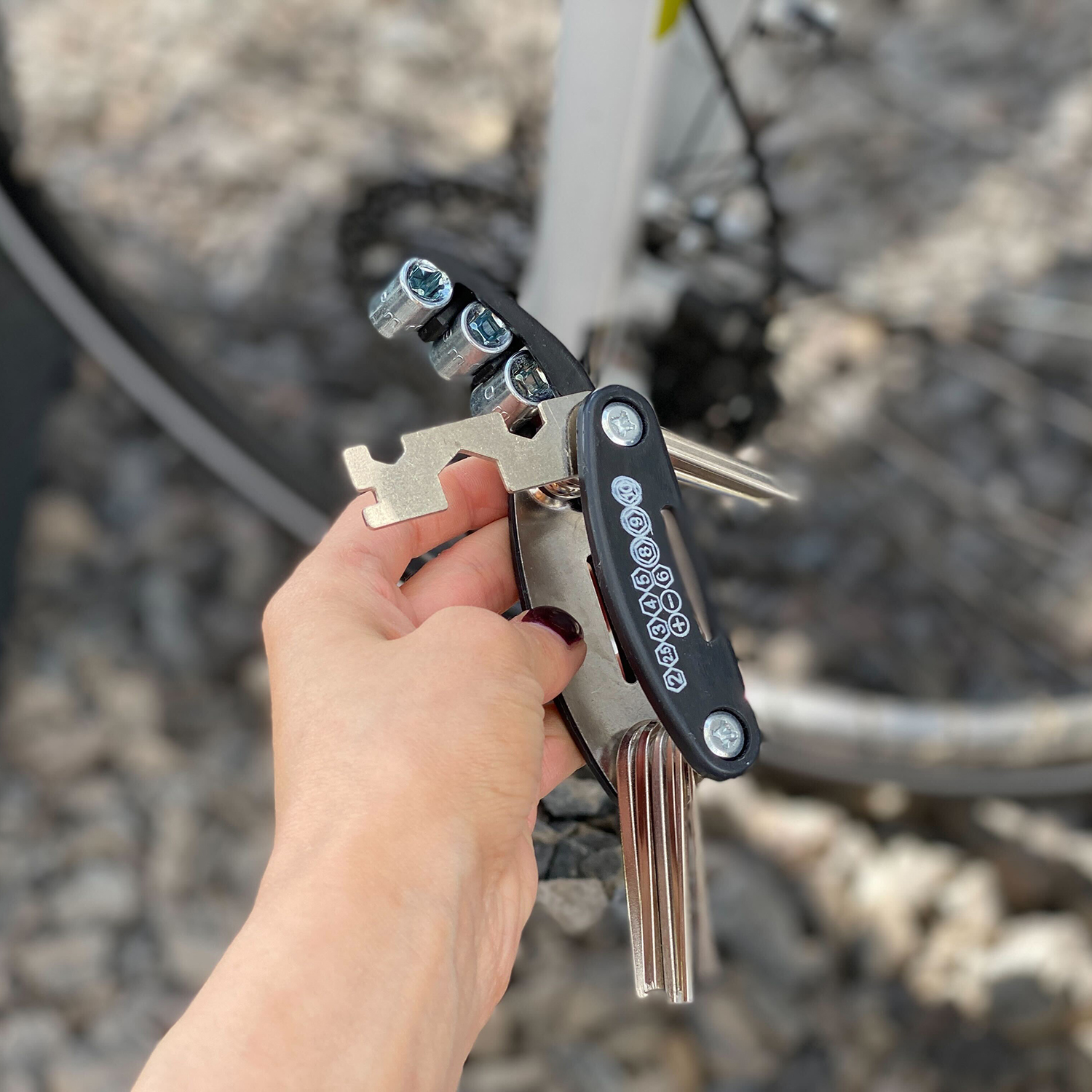 Eine Hand hält ein Multitool für ein Fahrrad. Das Werkzeug ist schwarz und silber mit mehreren Funktionen.