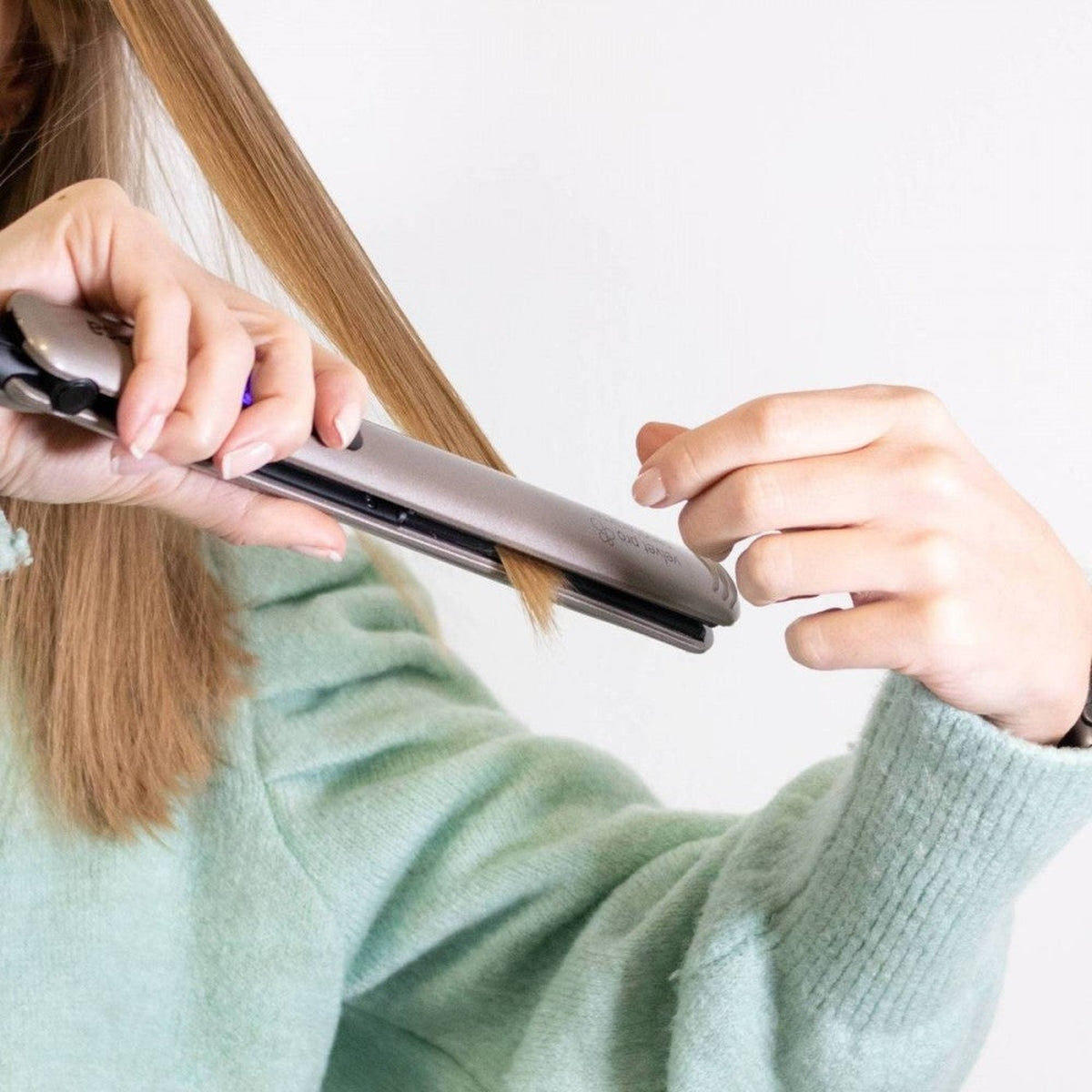 Una mujer usando una plancha para el pelo en su cabello.