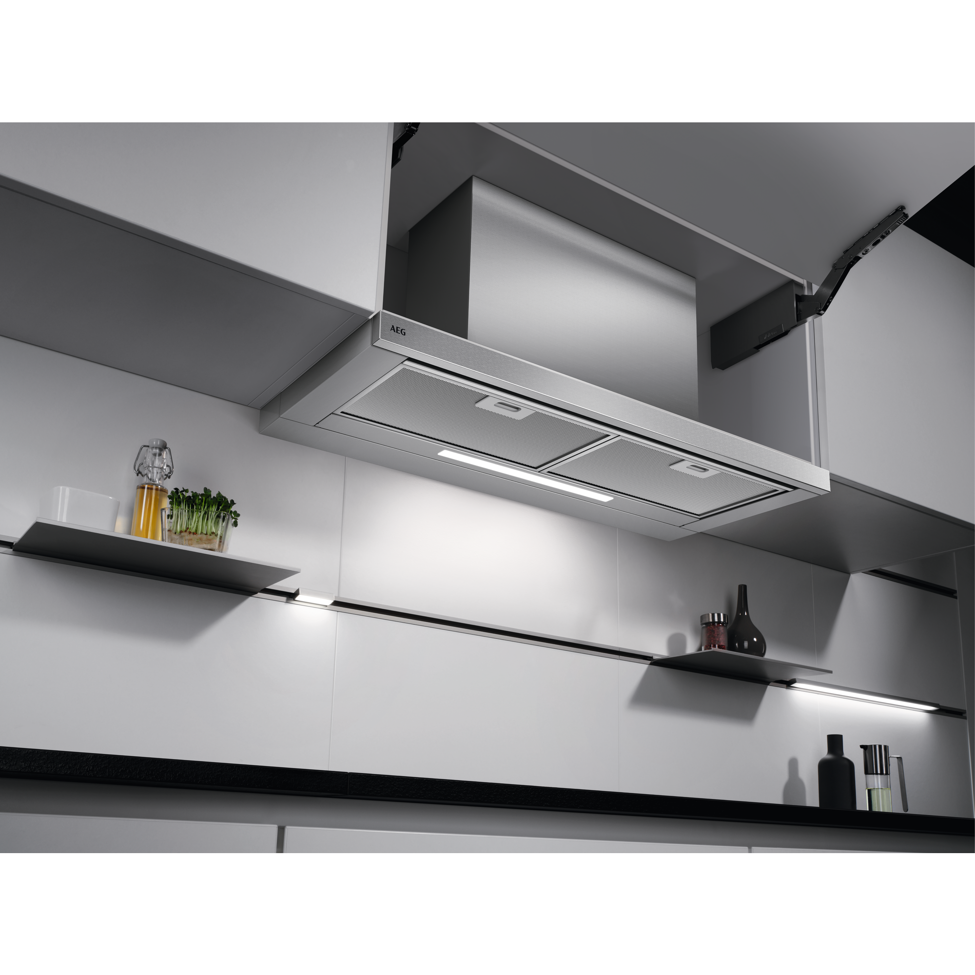 Cucina con cappa in acciaio inox. I mobili sono bianchi, con piani di lavoro neri.