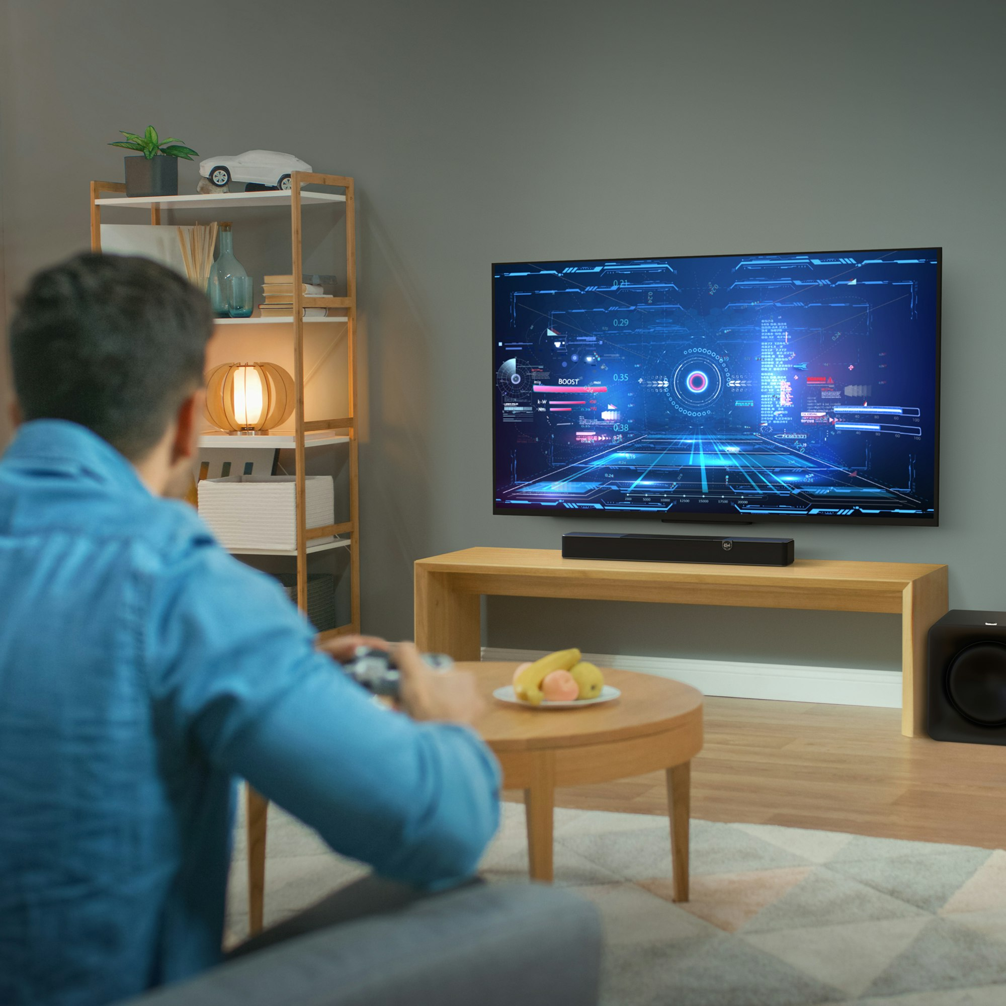 Mężczyzna siedzi, ogląda telewizję. Czarny soundbar i subwoofer pod telewizorem.