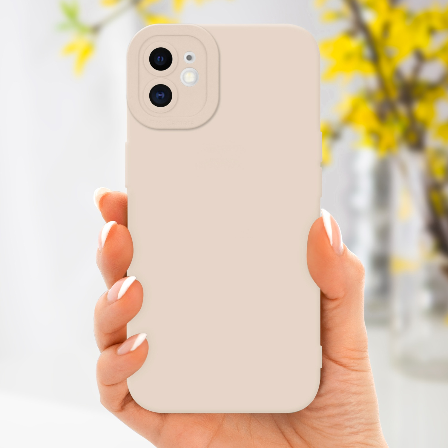 Una mano che tiene una custodia beige per telefono con un ritaglio per la fotocamera, su uno sfondo sfocato di fiori gialli.