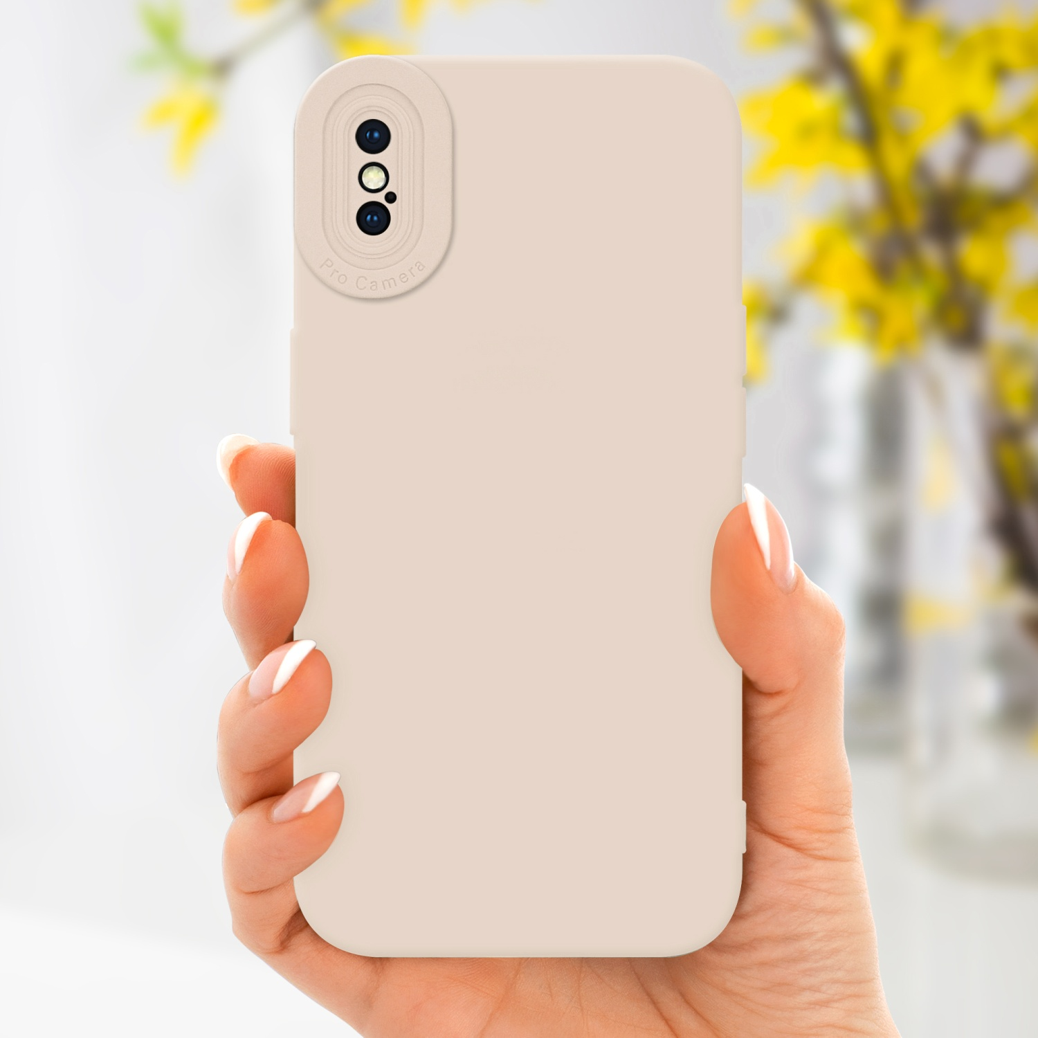 Una mano che tiene una custodia beige con una configurazione a tripla fotocamera, con uno sfondo sfocato di fiori gialli.