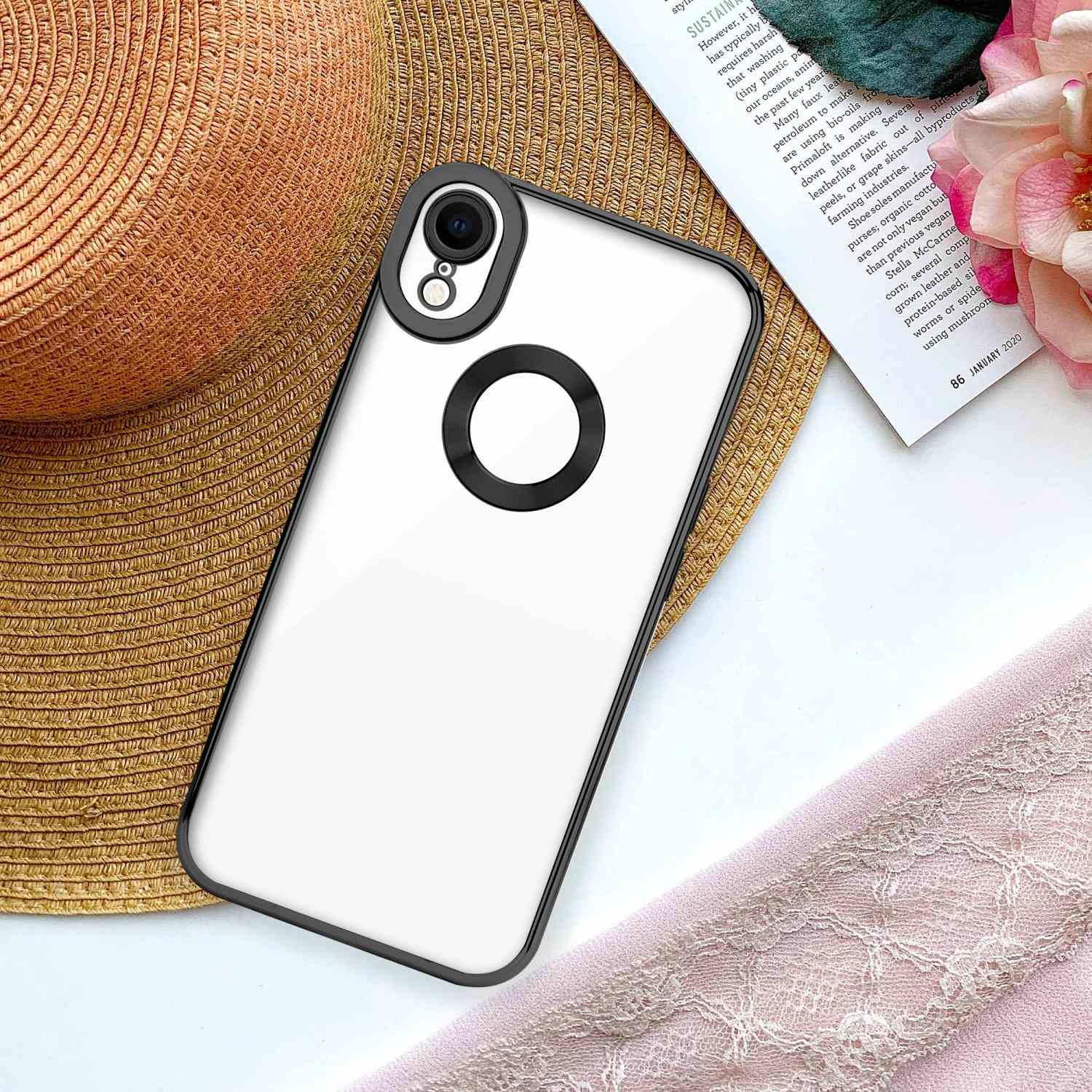 Una custodia per telefono con retro trasparente è su un cappello e un libro, un tessuto rosa sullo sfondo.