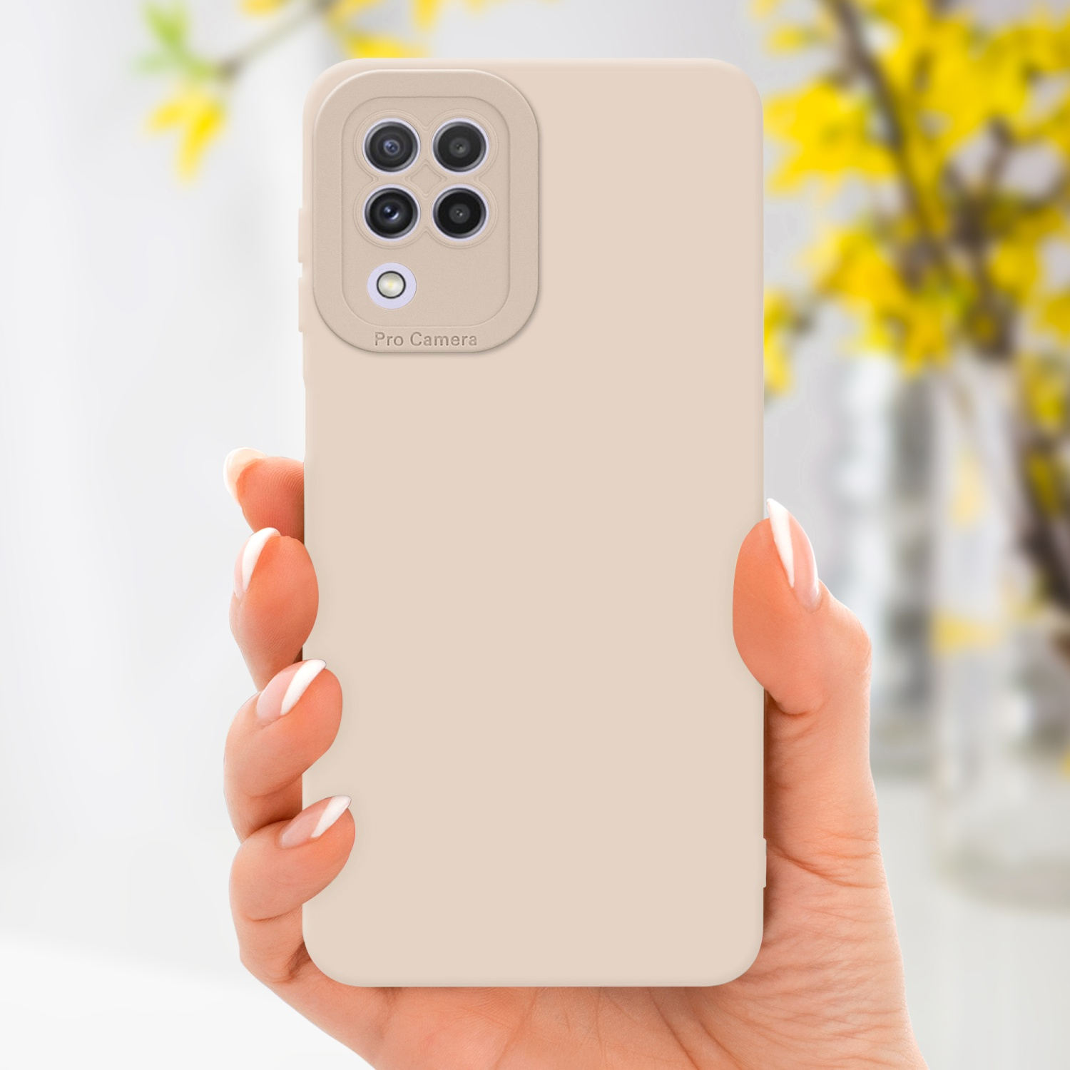 Main tenant une coque de téléphone beige avec une bosse pour la caméra. Fleurs jaunes floues en arrière-plan.