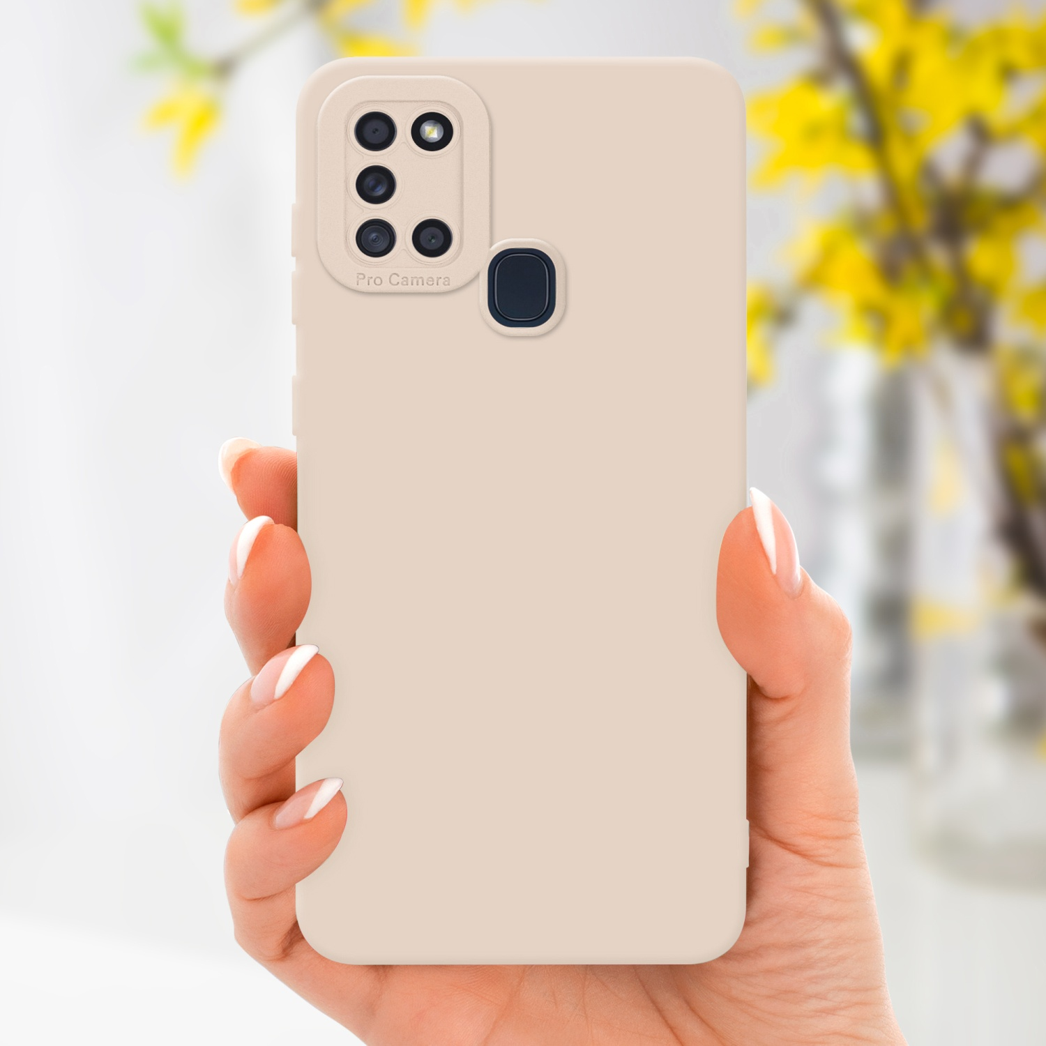 Main tenant une coque beige avec bosse caméra et fleurs jaunes en arrière-plan.