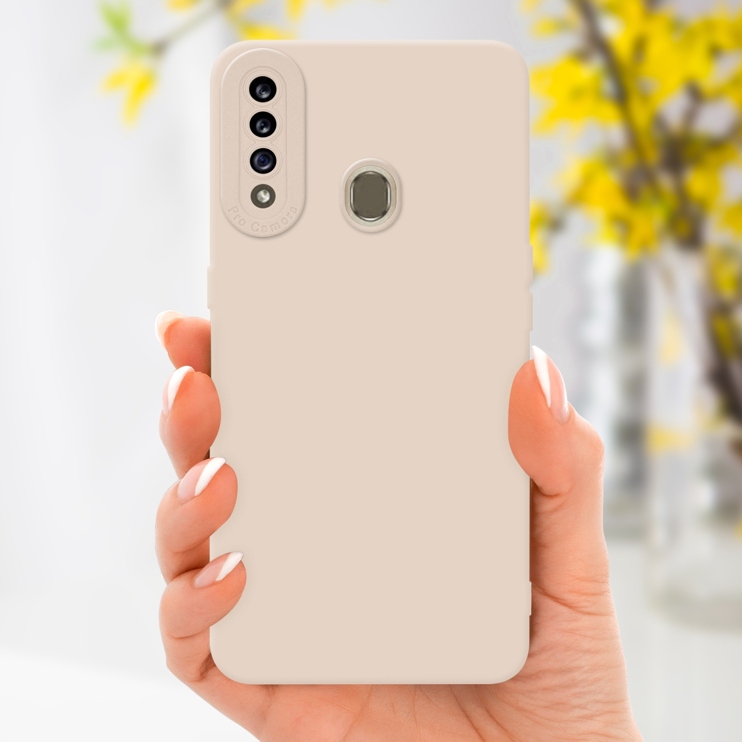 Hand hält Telefon in beigem Gehäuse. Telefon hat Dreifach-Kamera. Gelbe Blumen im Hintergrund.