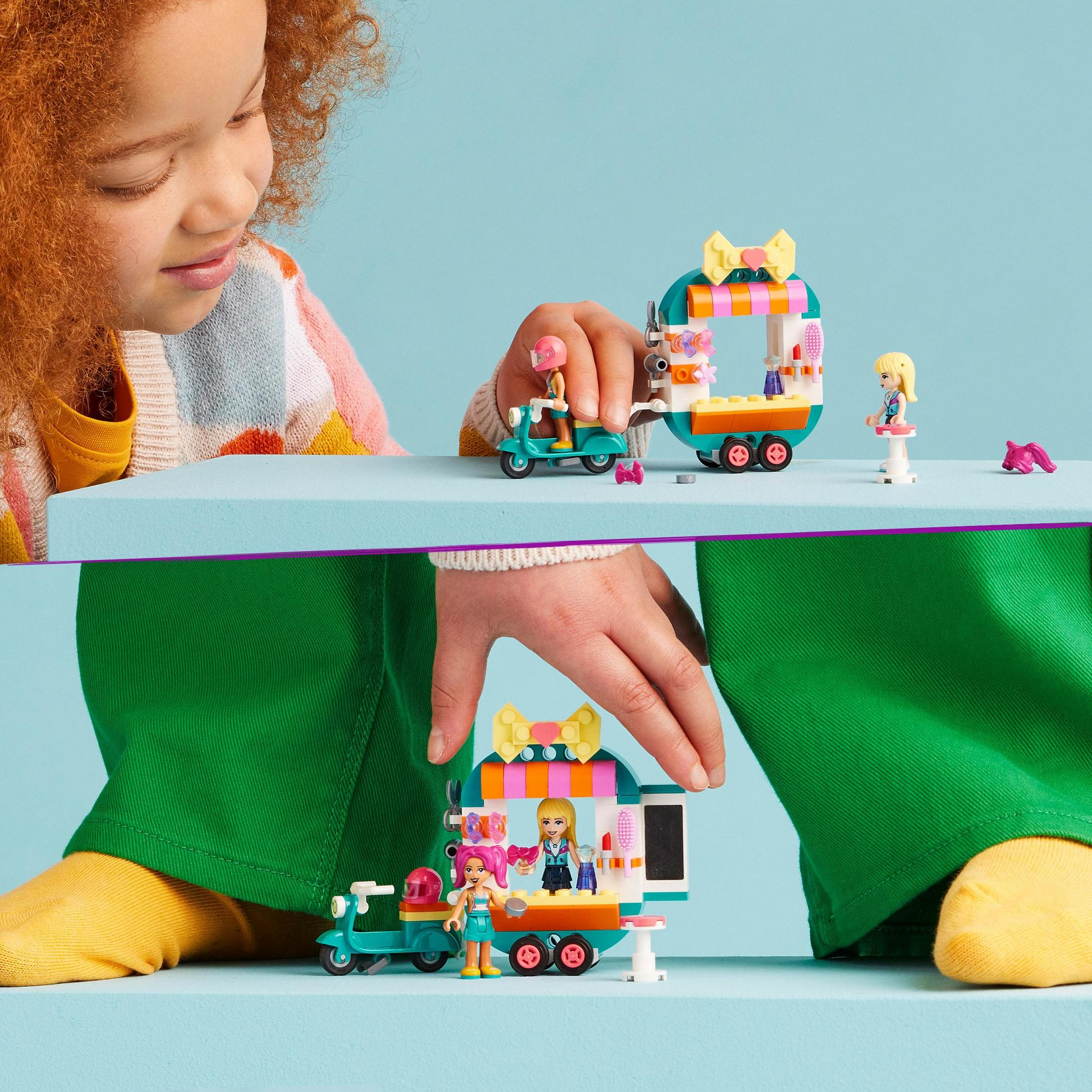Un niño jugando con un set de Lego Friends con un camión de comida y un scooter.