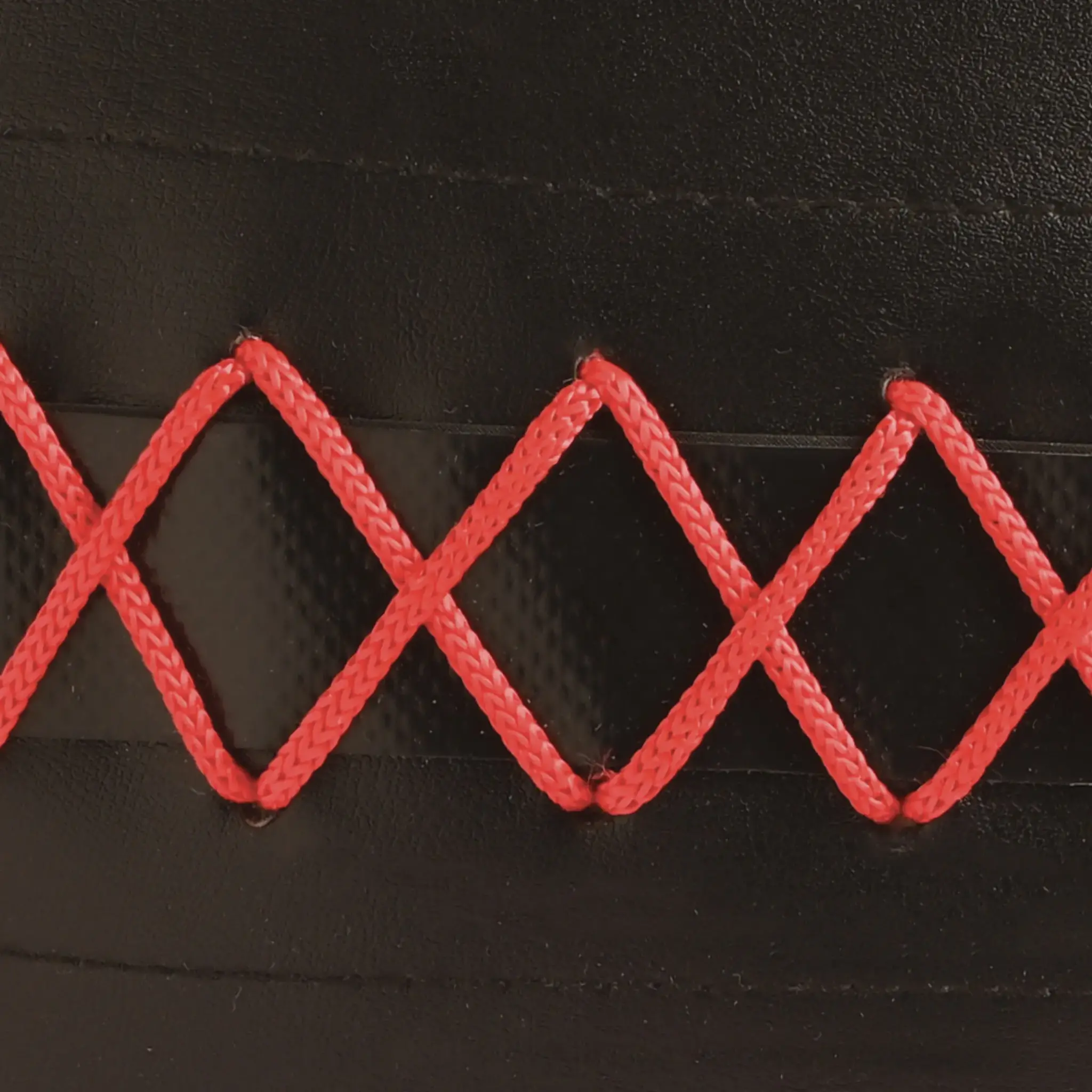 Close-up van zwart materiaal gestikt met rood garen in een ruitpatroon.