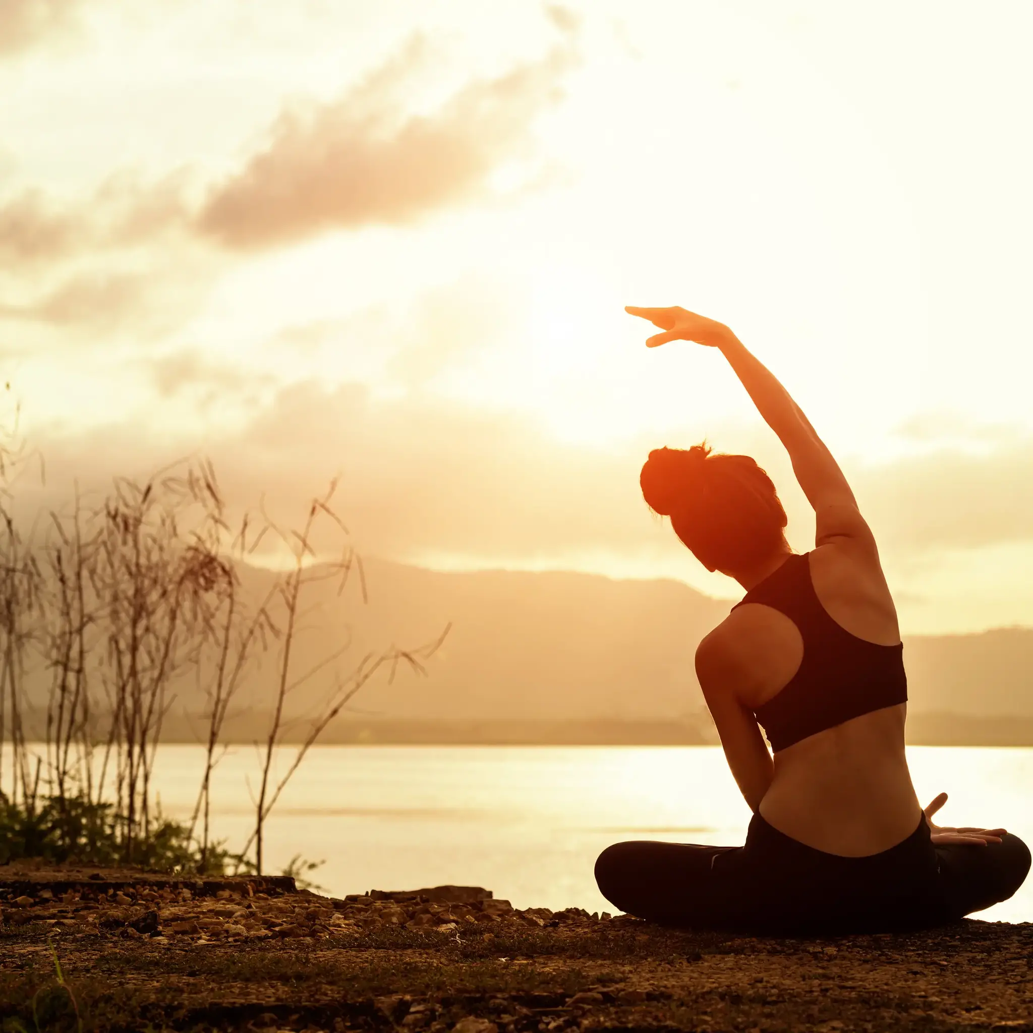 Woman doing yoga by a lake at sunset.