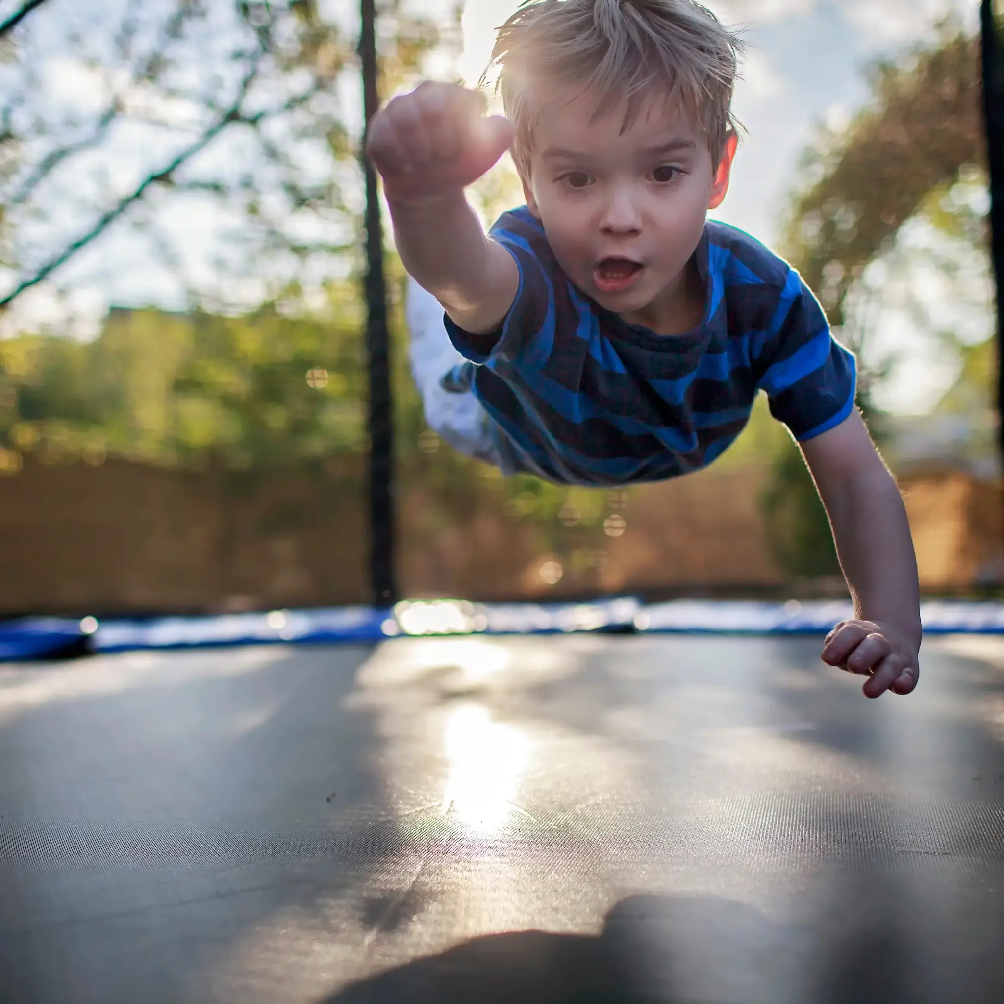 Een jongen in de lucht op een trampoline, wijd open ogen, armen en benen uitgestrekt, tegen een groene achtergrond.