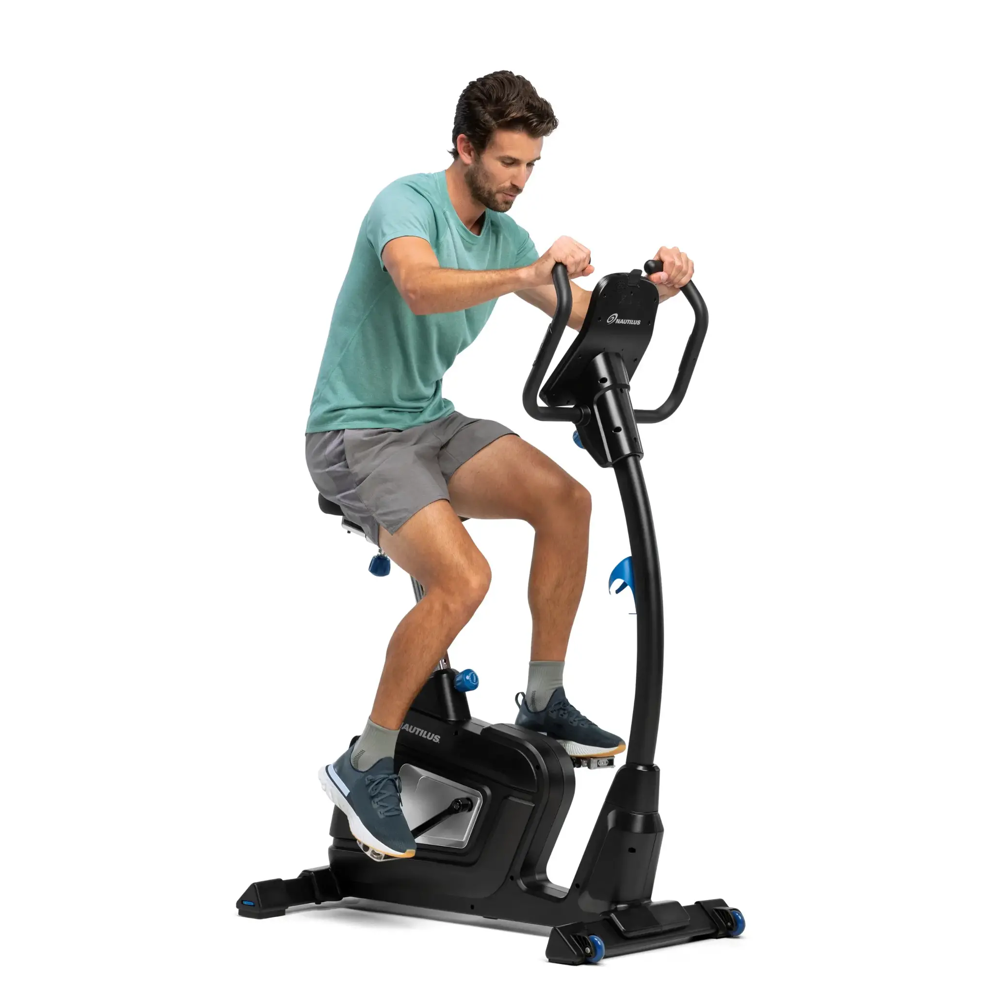 Mann auf einem Heimtrainer, trainierend. Weißer Hintergrund. Grünes Hemd, graue Shorts.