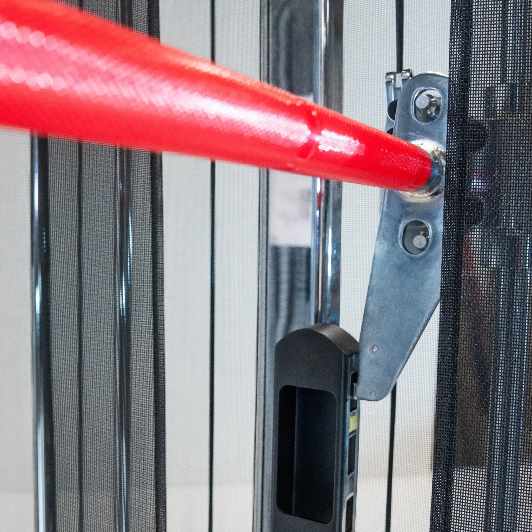 Nahaufnahme eines Sicherheitstores mit roter Stange und schwarzem Griff. Das Tor ist metallisch.