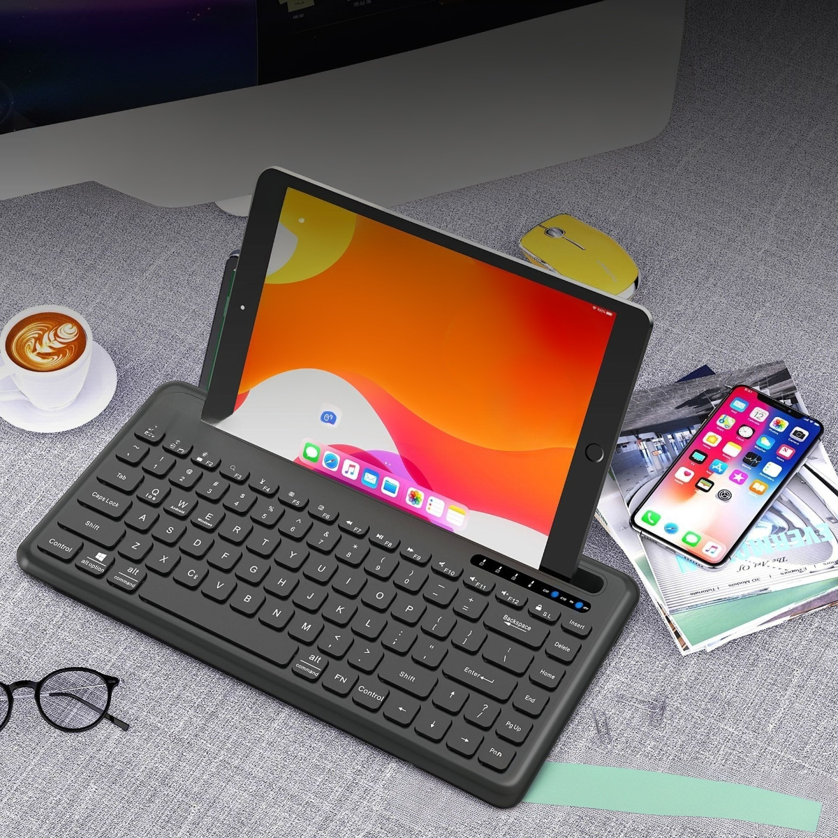 Ein iPad mit Tastaturhülle, ein Telefon, eine Maus und eine Tasse Kaffee auf einem Schreibtisch.