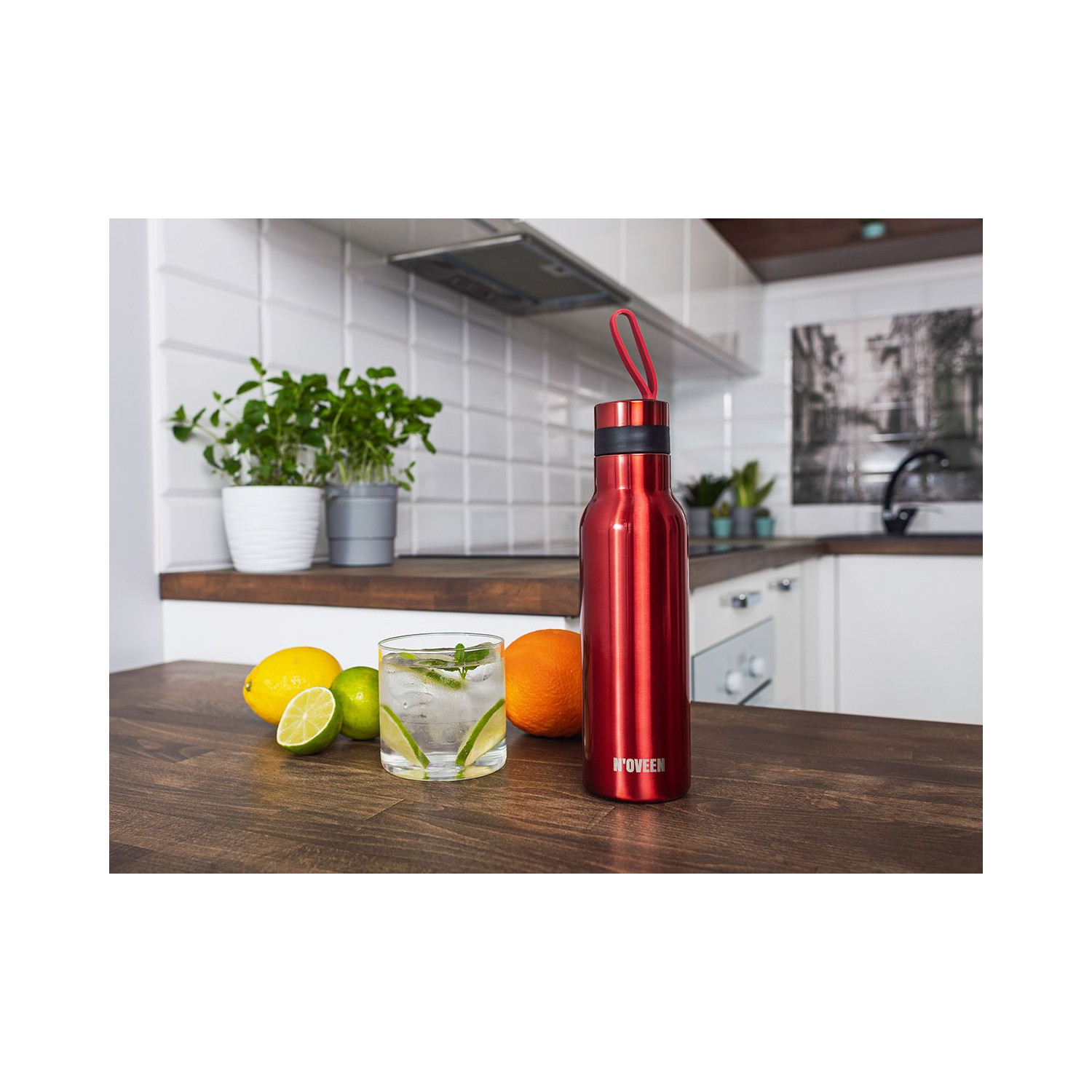 Eine rote Wasserflasche und ein Glas Wasser mit Limette und Minze auf einem Holztisch.
