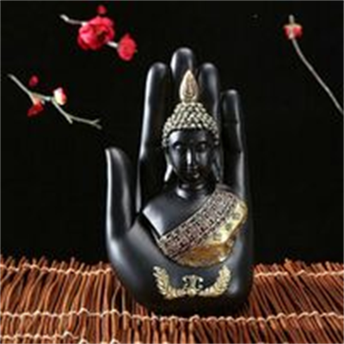 Eine schwarze handförmige Buddha-Statue mit goldenem Gewand, auf brauner Webfläche.
