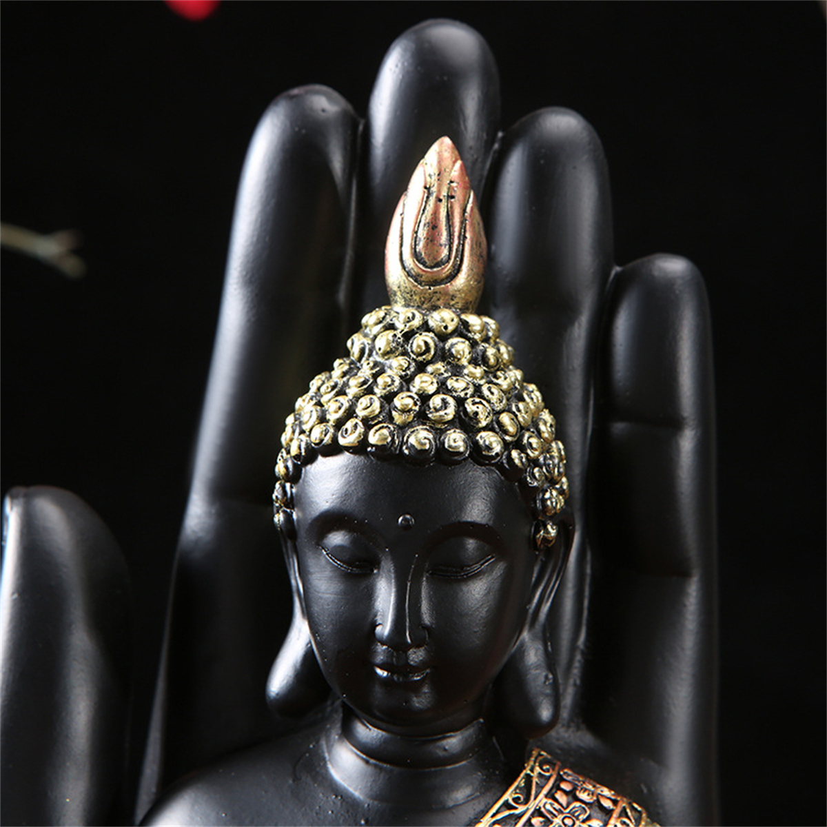 Schwarze Buddha-Statue mit goldenen Akzenten, auf schwarzer Hand, dunkler Hintergrund.