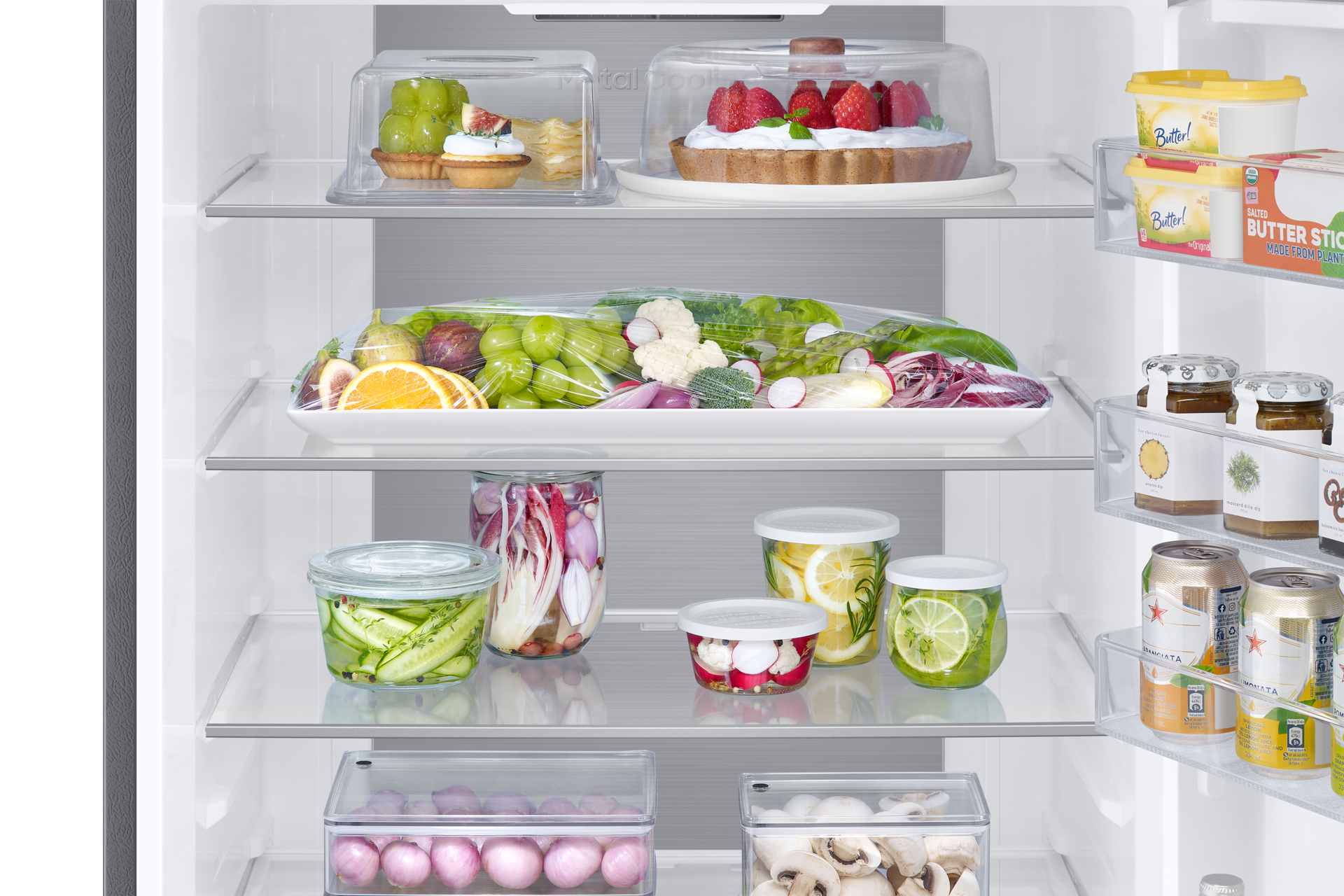 Nahaufnahme von Kühlschrankregalen mit Lebensmitteln: Gemüse, Obst, Gläser, Butter.