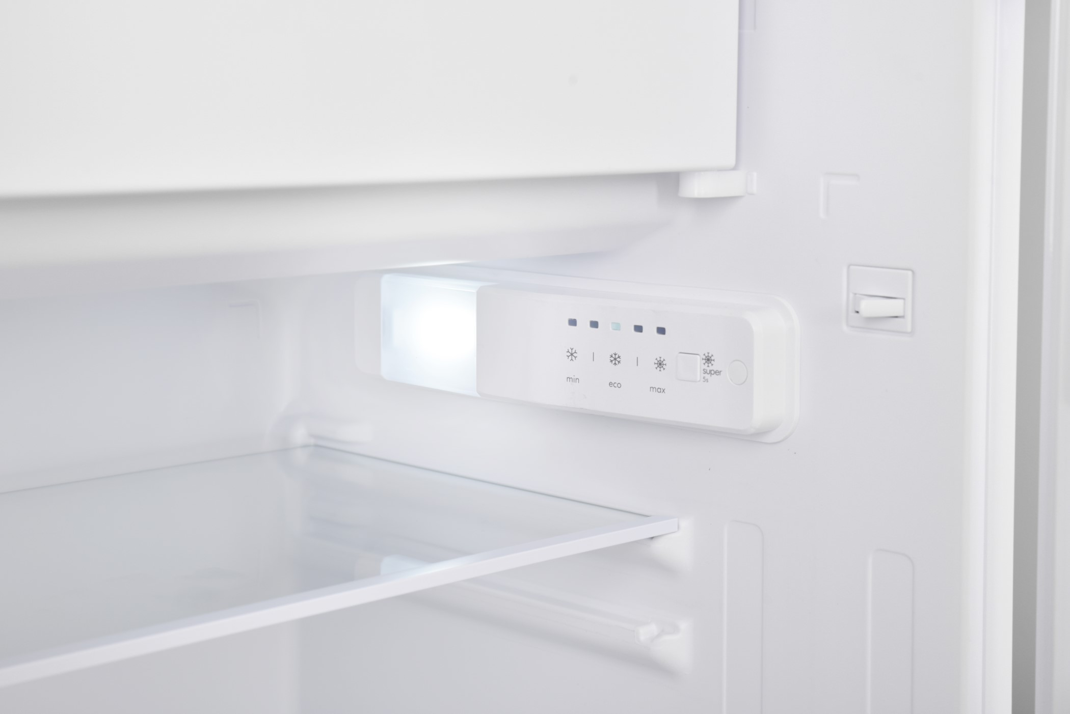 Inside a white refrigerator: shelf, light, and control panel with settings for temperature.