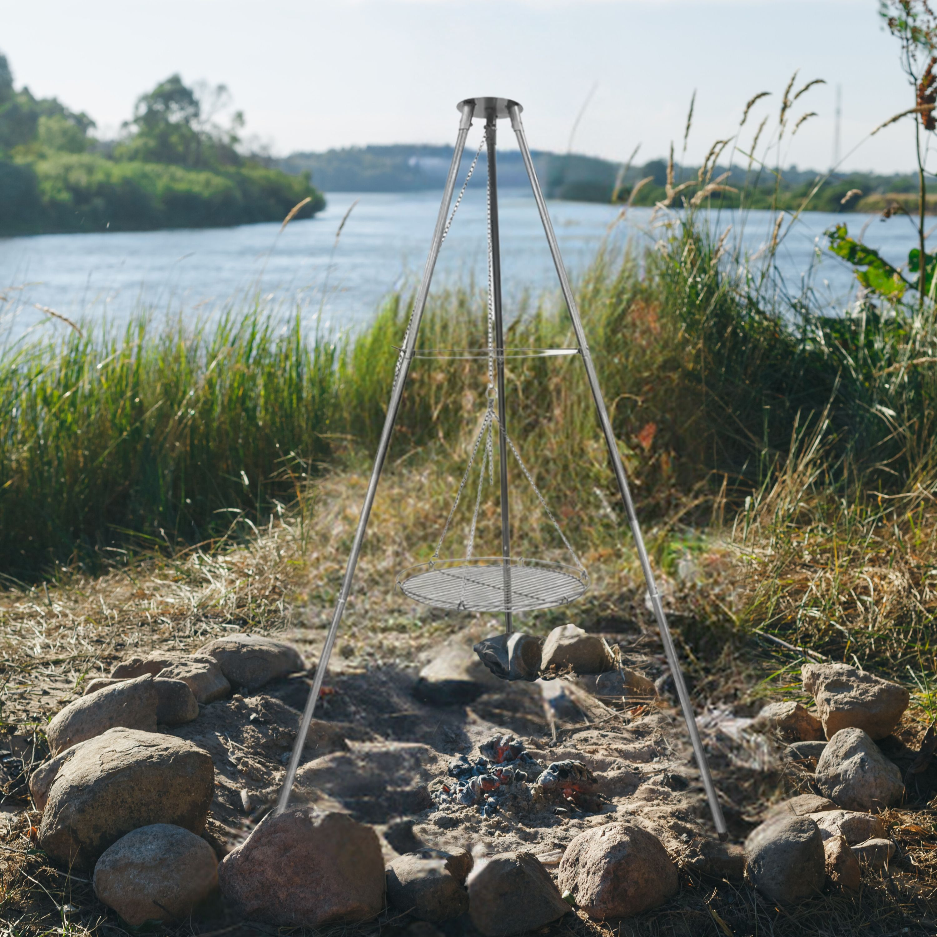 Ein Metallstativ mit Grill über einer Feuerstelle. Im Hintergrund ein See und hohes Gras.