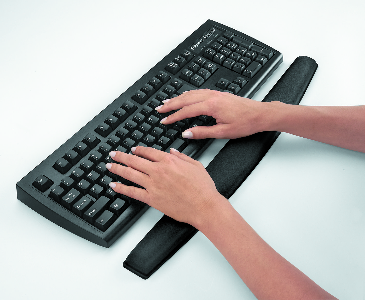 Mani che digitano su una tastiera nera con poggiapolsi su sfondo bianco.