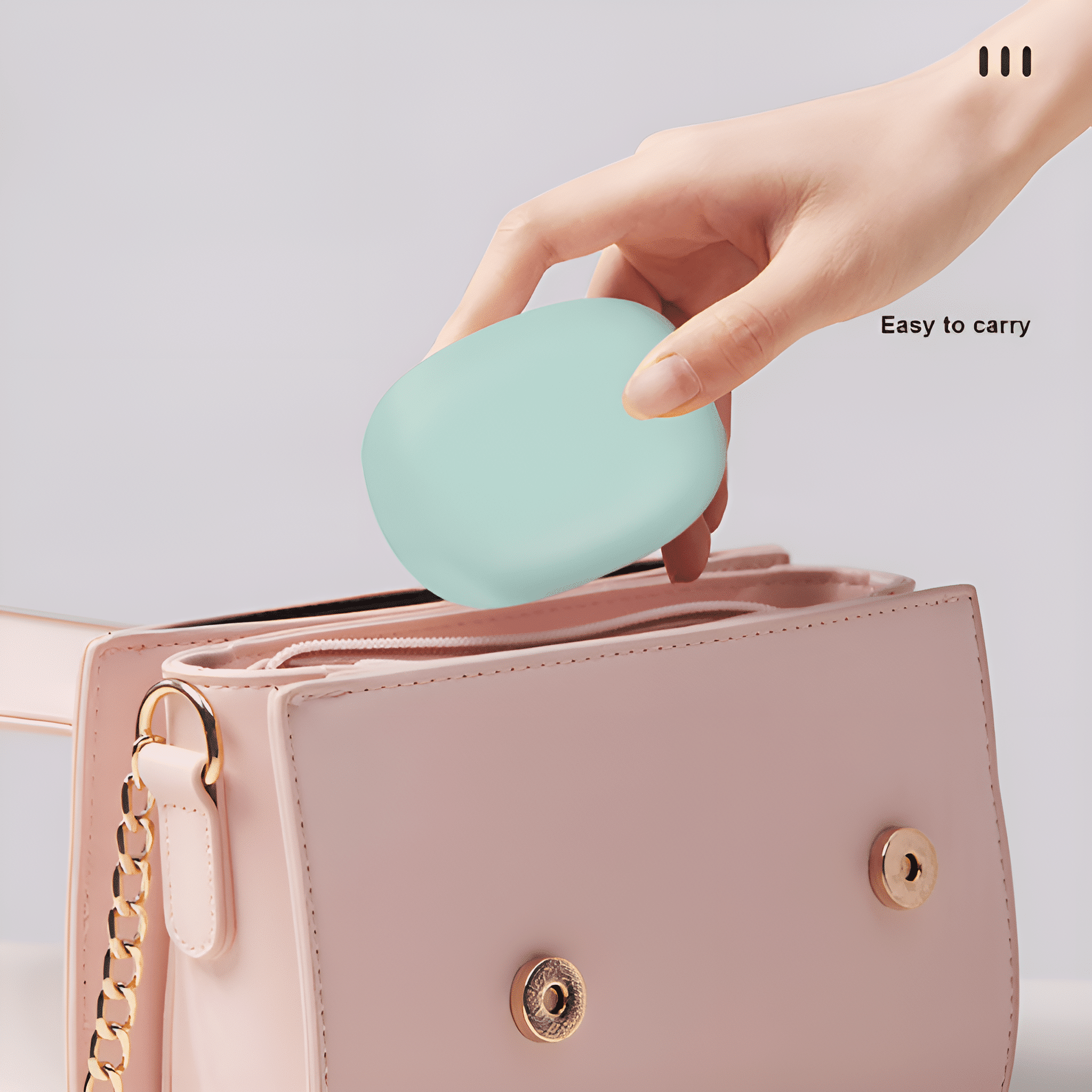 Eine Hand hält ein grünes Gesichtsreinigungsgerät über einer rosa Handtasche.