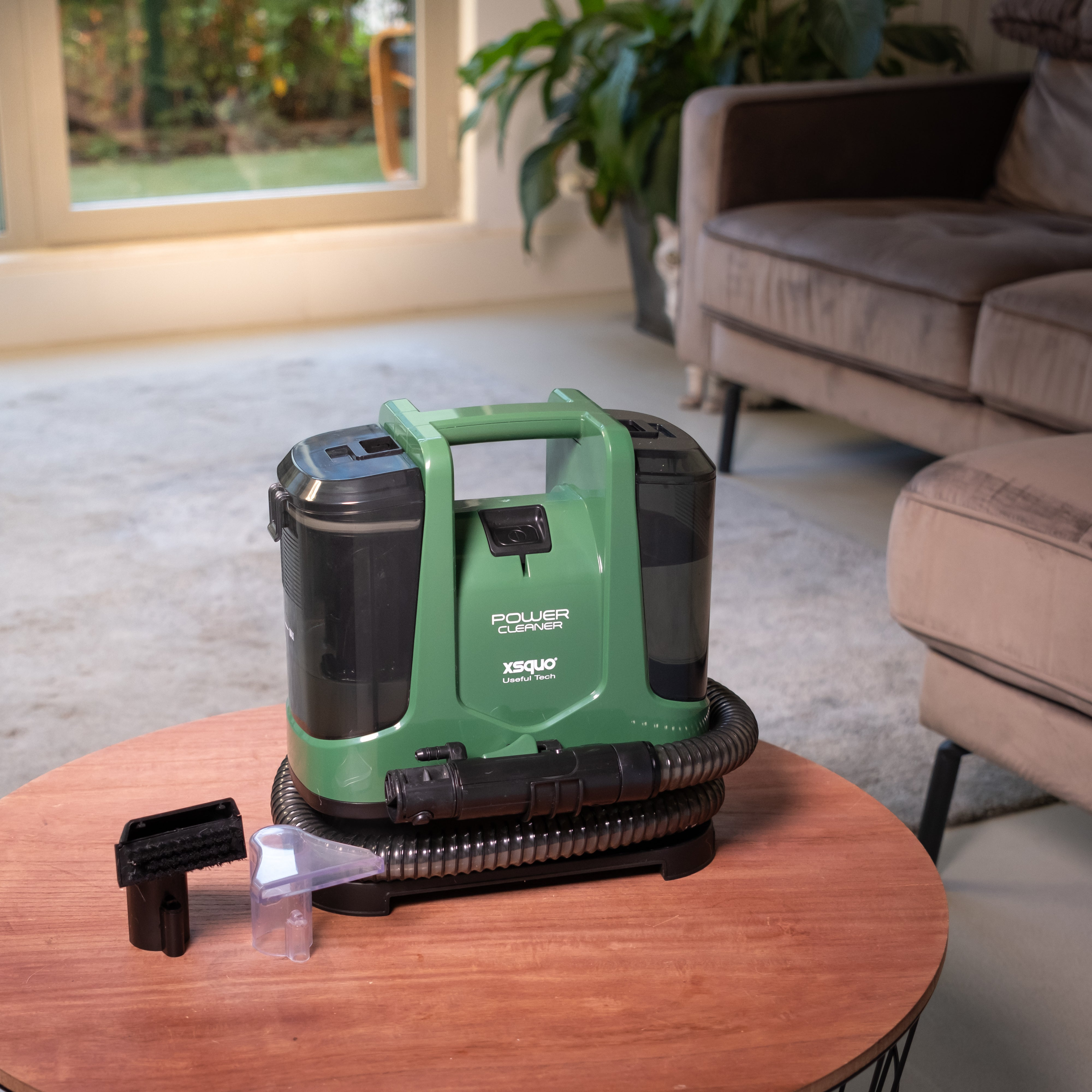 Aspiradora portátil verde y negra en una mesa marrón con accesorios, en una sala de estar.