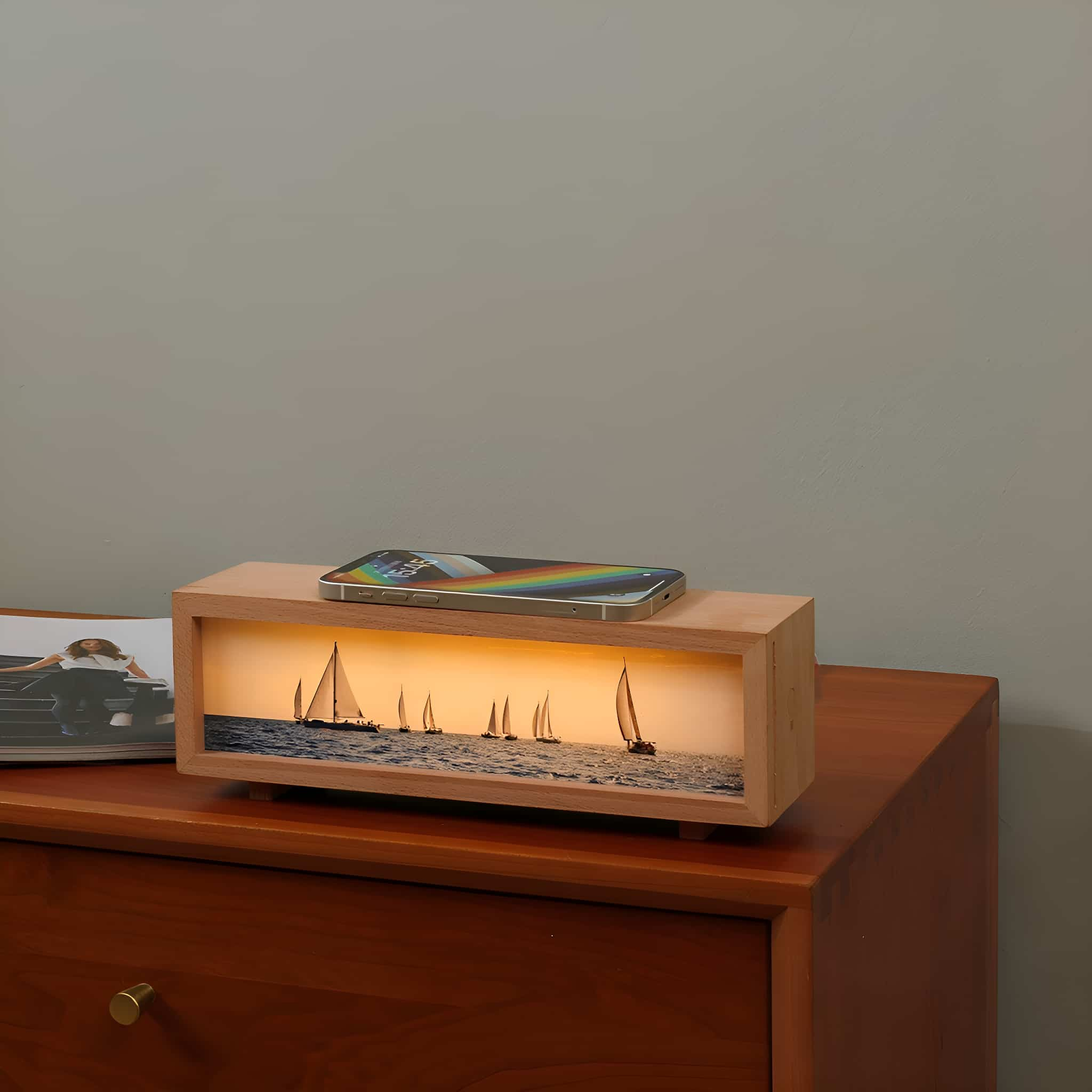 Eine hölzerne Lichtbox mit einem Telefon oben, das Segelboote bei Sonnenuntergang zeigt.