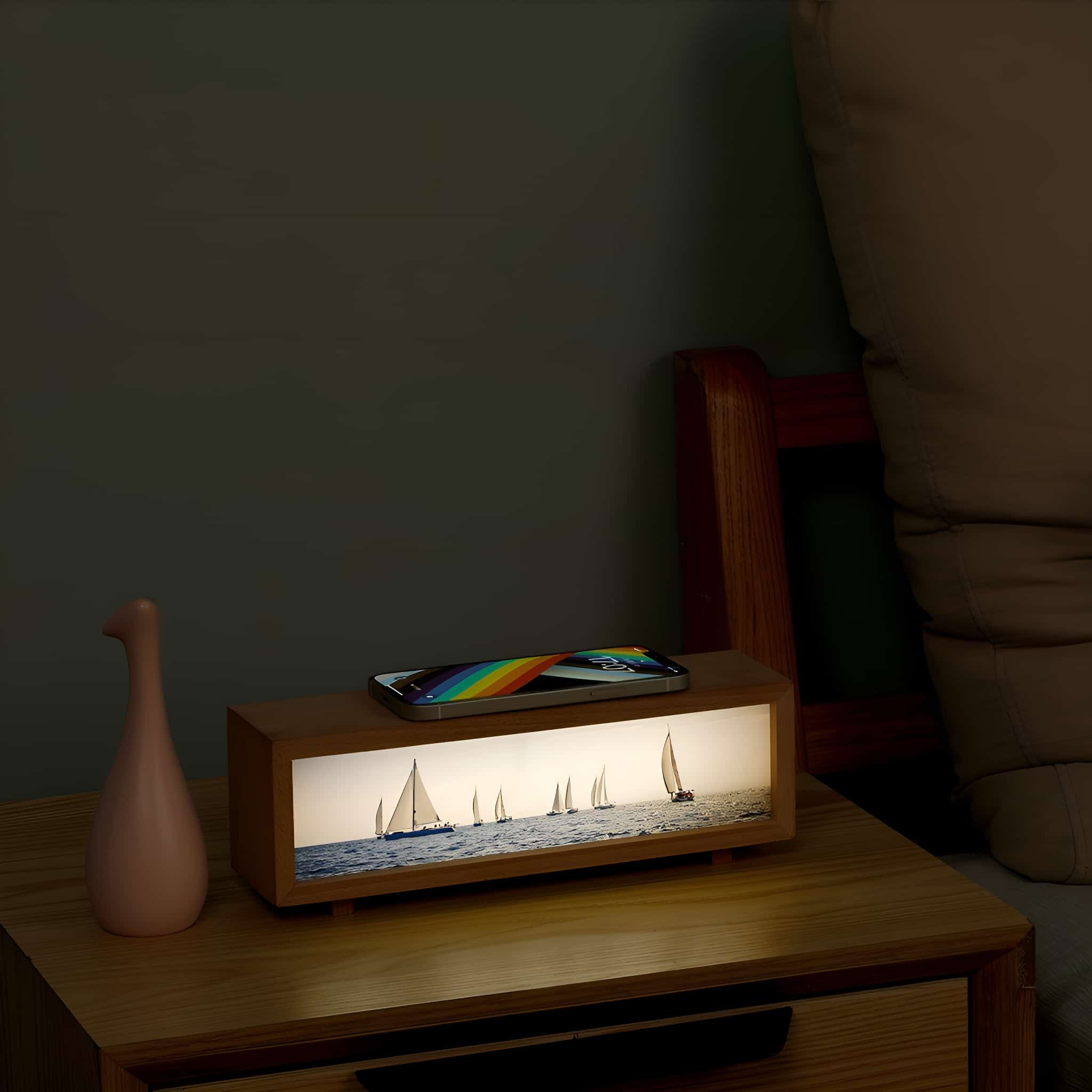 Ein hölzerner Nachttisch mit einem Telefon, das eine Segelszene zeigt, mit Regenbogen und Blumenvase.