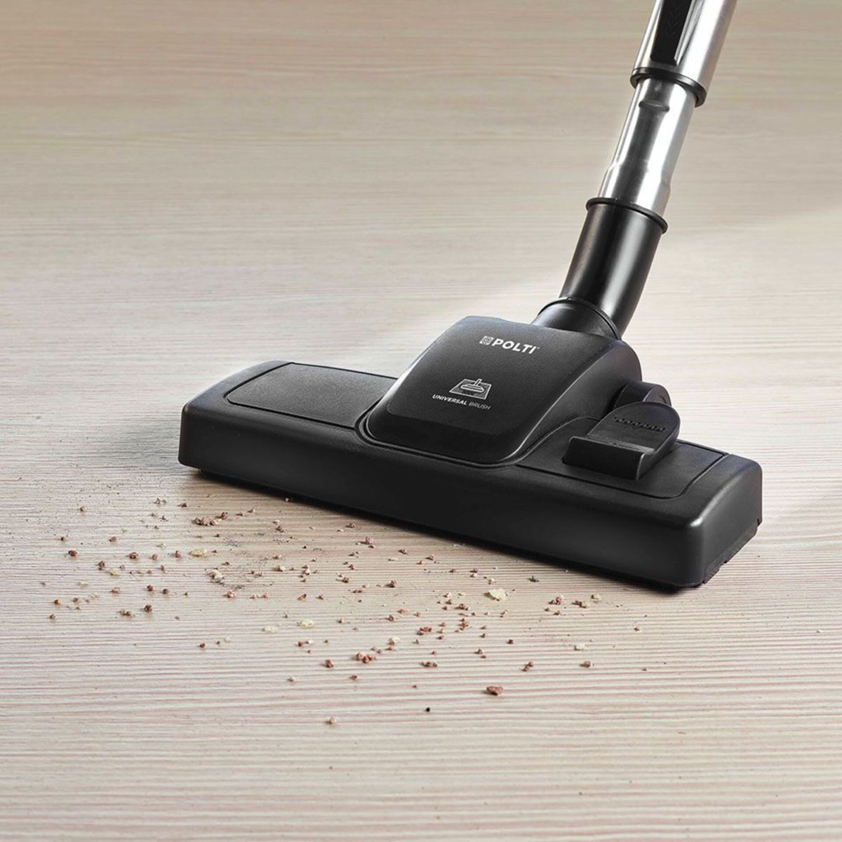 Czarna głowica odkurzacza na jasnej drewnianej podłodze. Na podłodze rozsiane zanieczyszczenia.