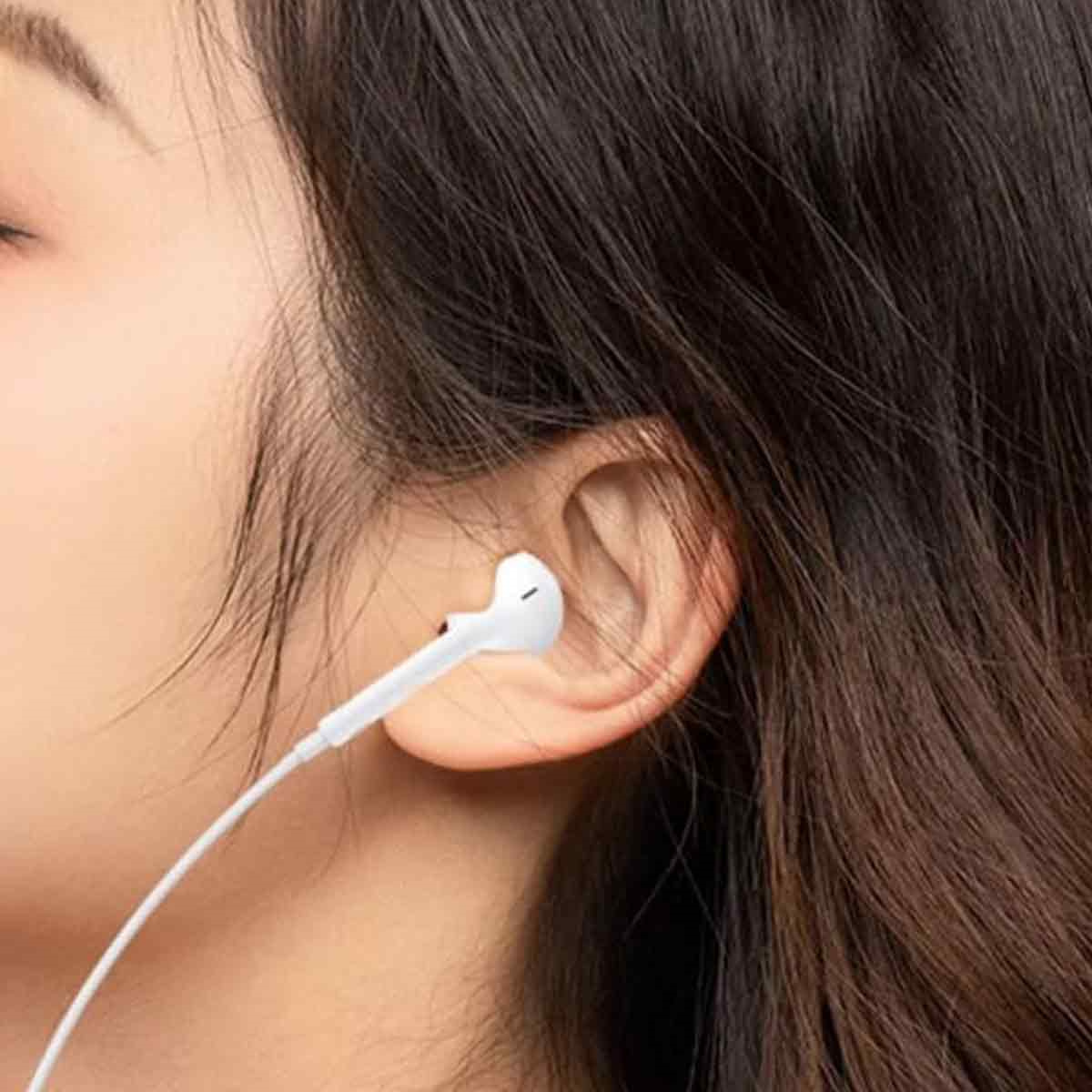 Ein Ohr einer Frau mit einem weißen Ohrhörer. Der Ohrhörer ist mit einem weißen Kabel verbunden.