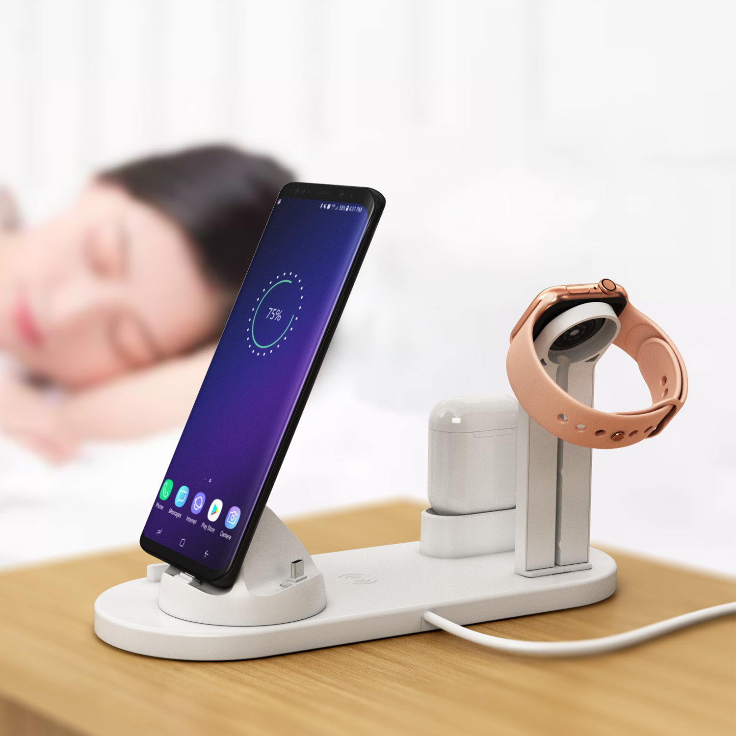 Una estación de carga con un teléfono, reloj y auriculares. Una persona está borrosa en el fondo.