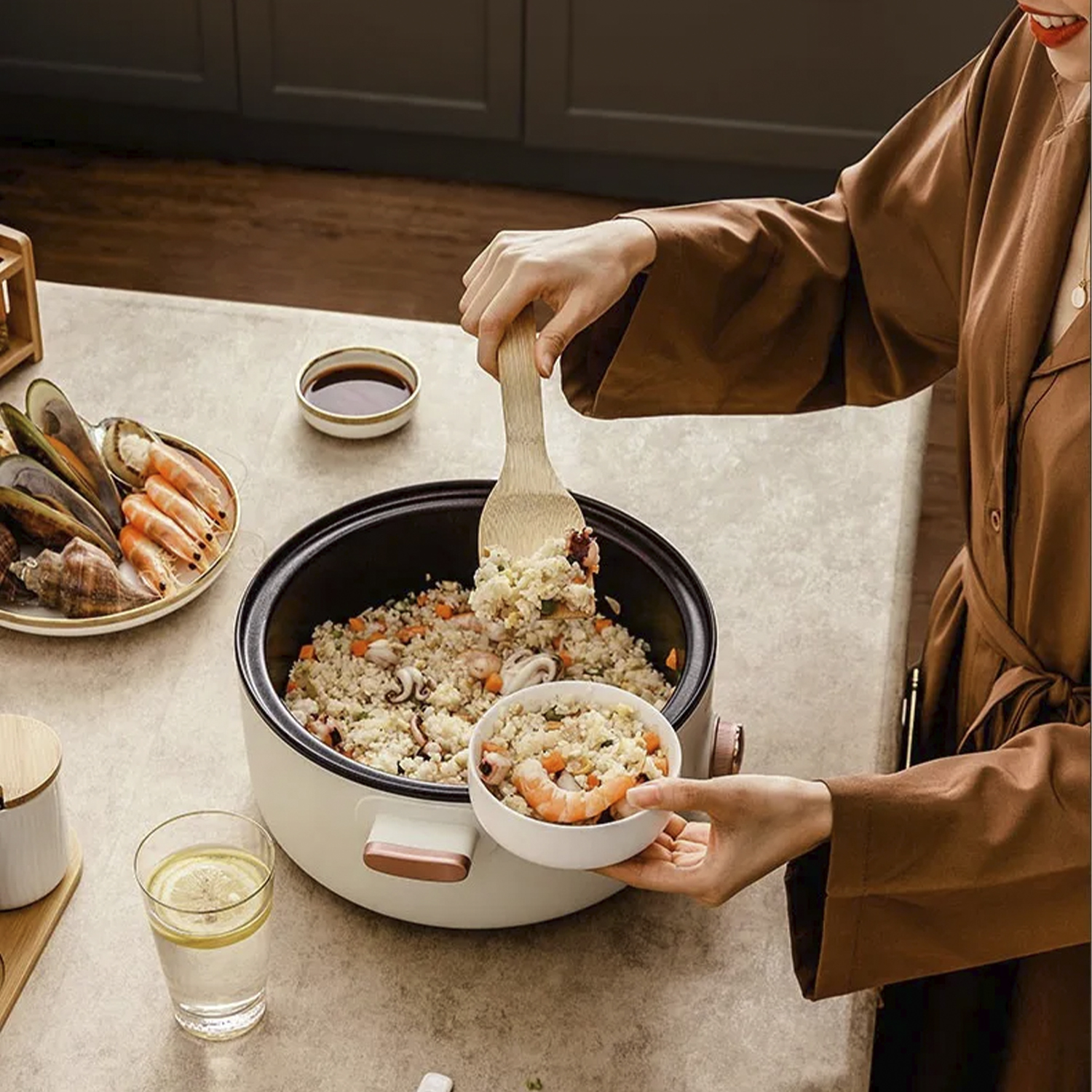 Una persona sostiene un cuenco de comida de una olla. Una olla de comida está en una mesa. Otras comidas están cerca.
