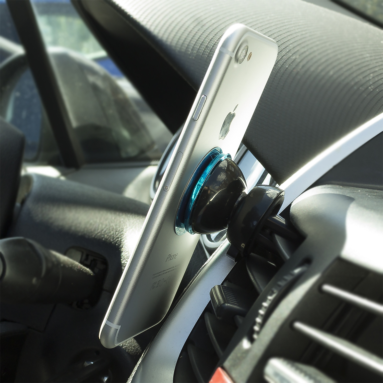 Un teléfono inteligente plateado montado en la ventilación de un coche, inclinado hacia el espectador.