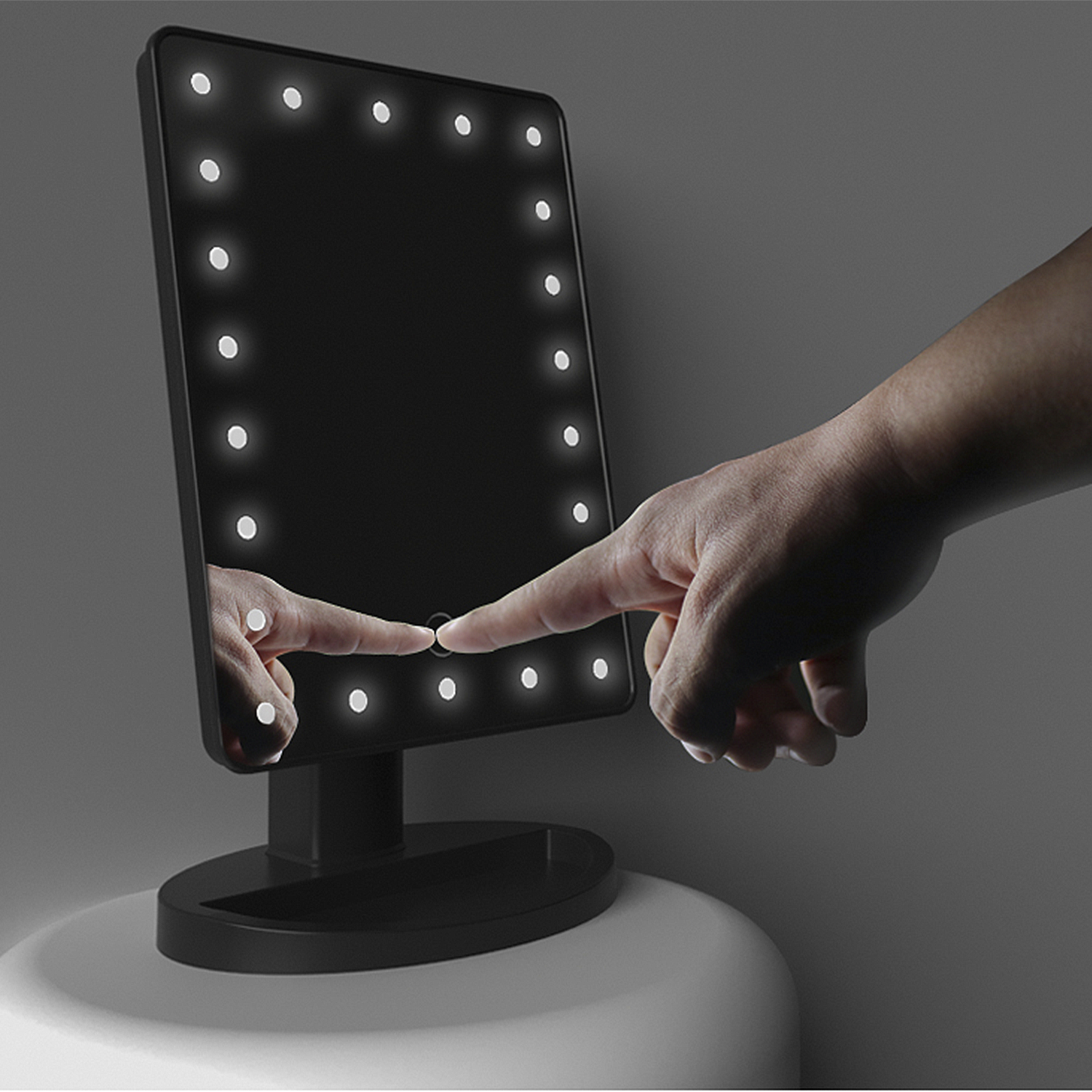 Un espejo de maquillaje negro iluminado con controles táctiles y una mano presionando la pantalla.