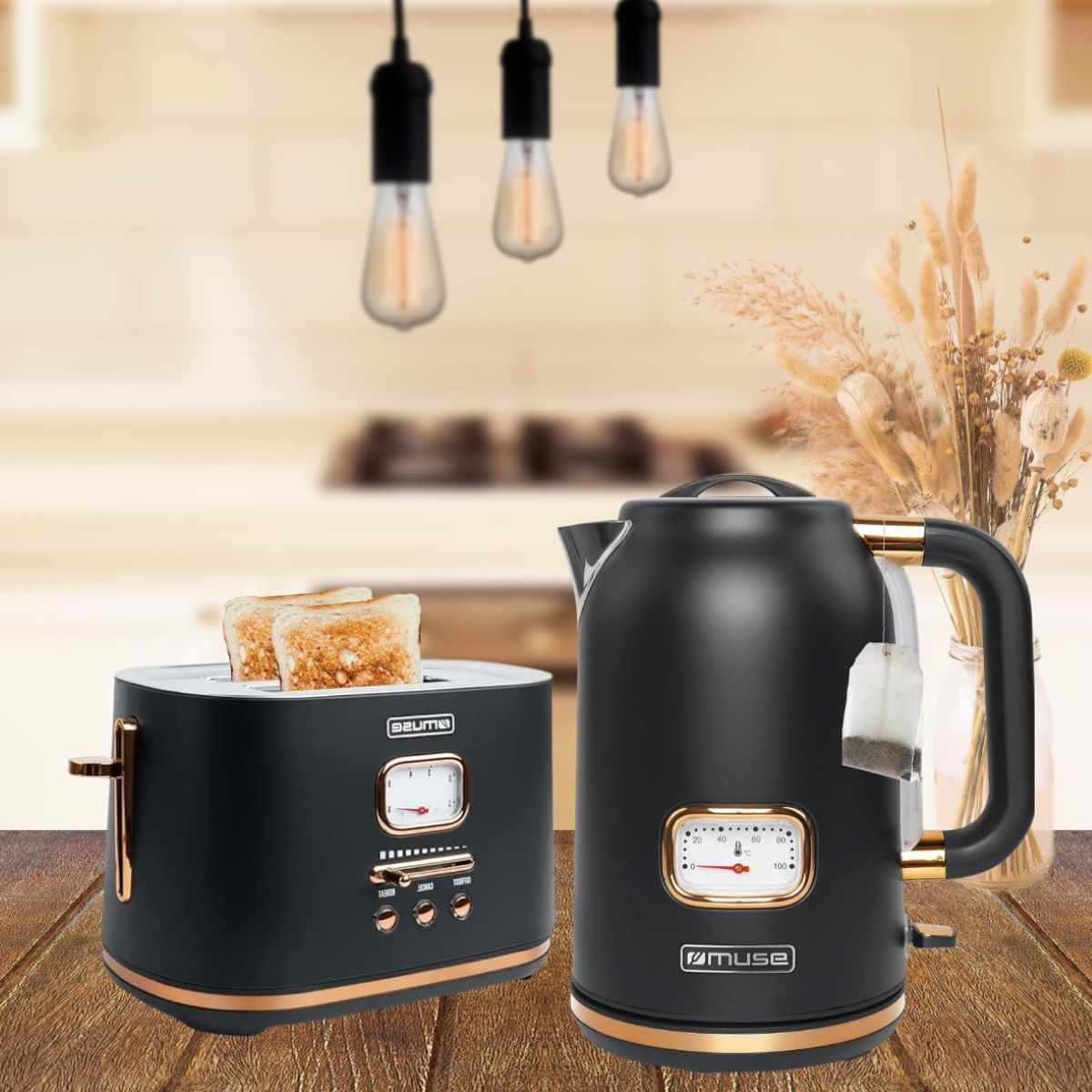 Czarny toster i czajnik ze złotymi akcentami na drewnianym stole, z wiszącymi światłami i aranżacją kwiatową.