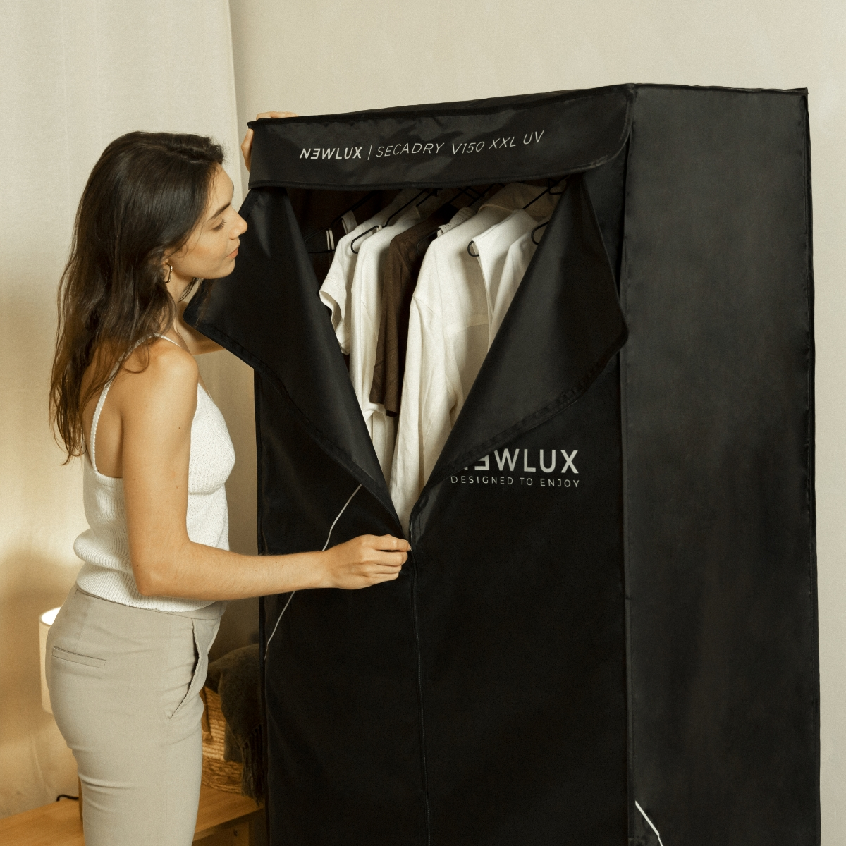 Mujer abriendo un armario secador negro. Ropa colgando dentro. La marca es visible.