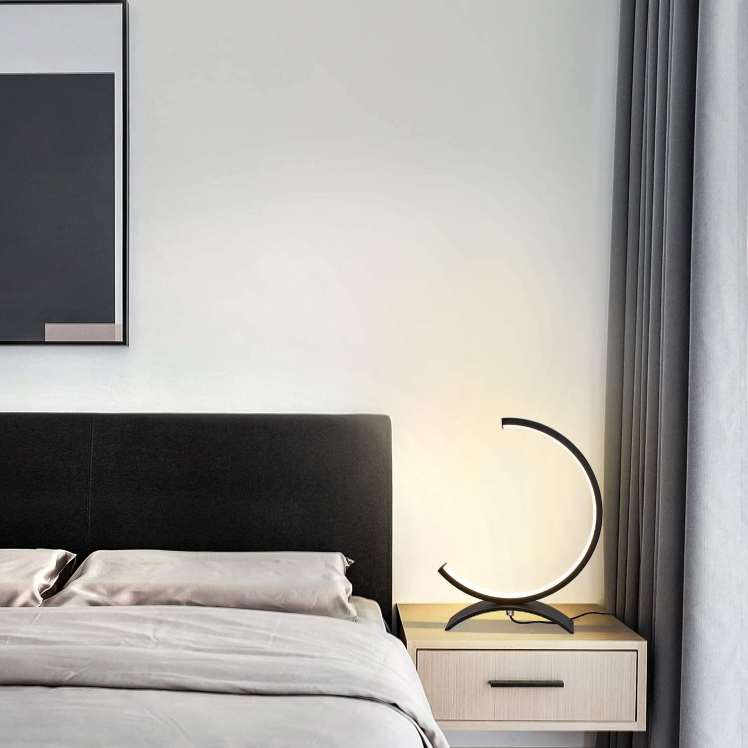 Czarna lampa w kształcie półkola na drewnianej szafce nocnej. Tłem jest biała ściana.