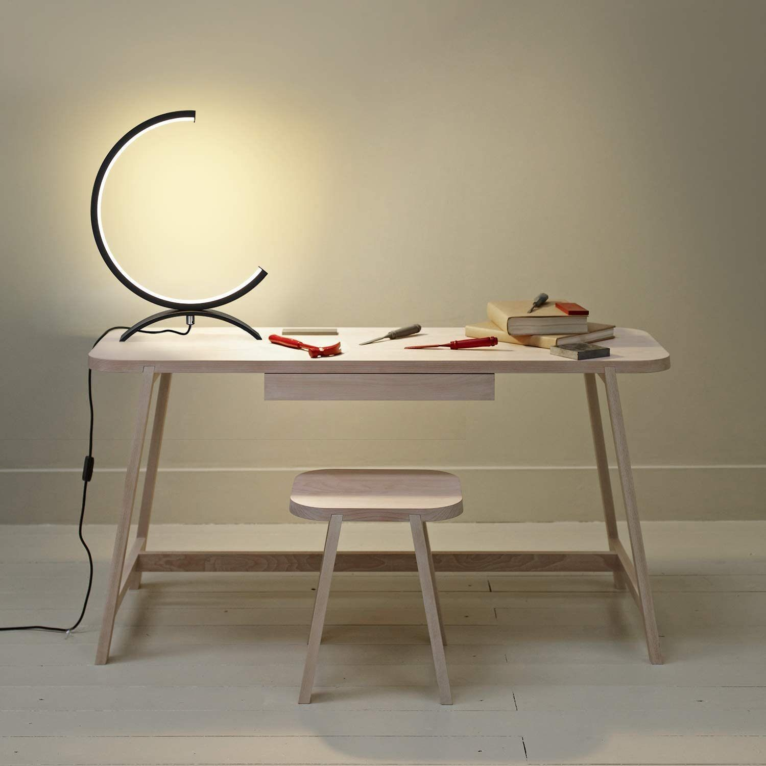 Biurko z lampą i stołkiem. Biurko ma narzędzia, książki. Lampa emituje światło.