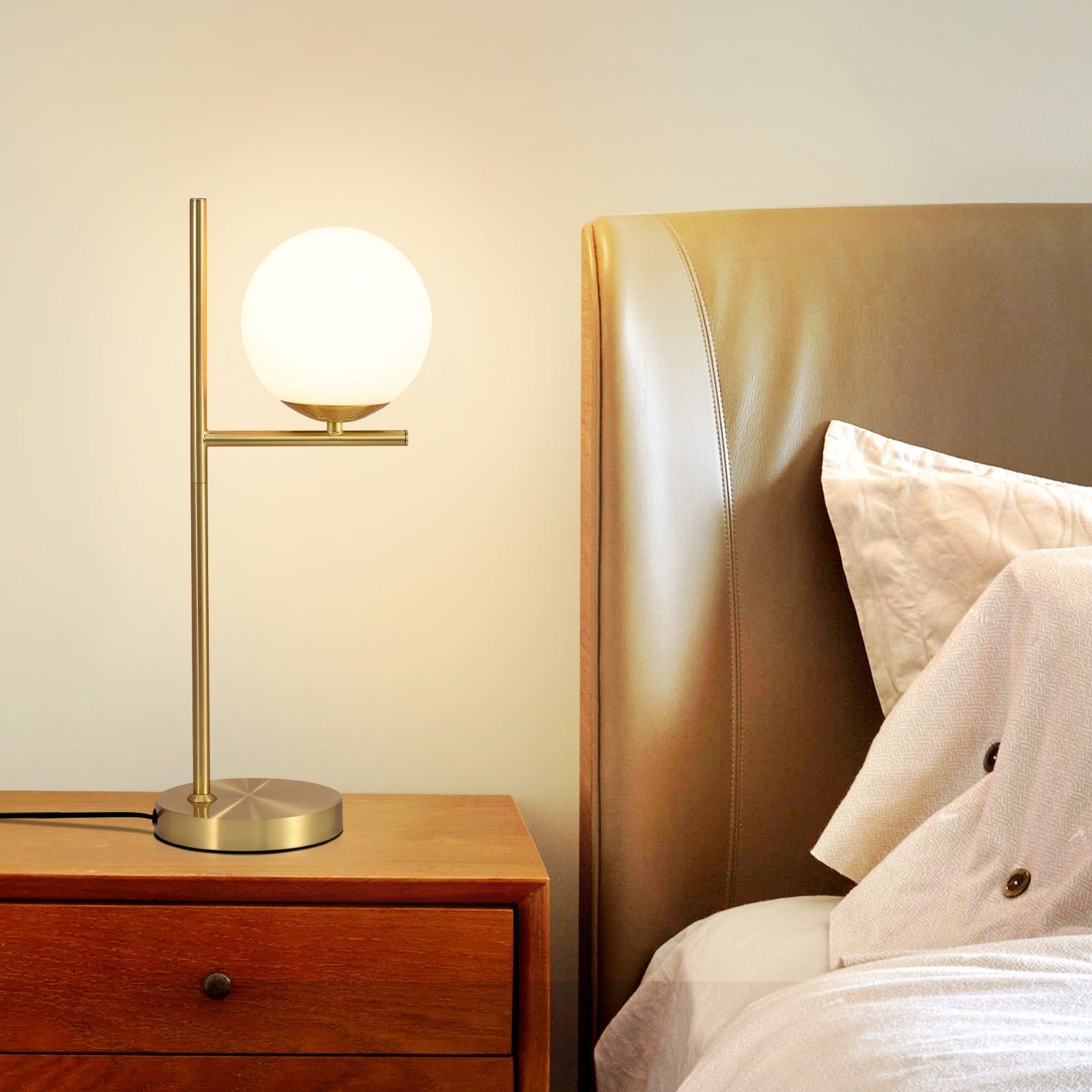 Złota lampa z białą kulą i drewnianym stolikiem nocnym z łóżkiem w tle.