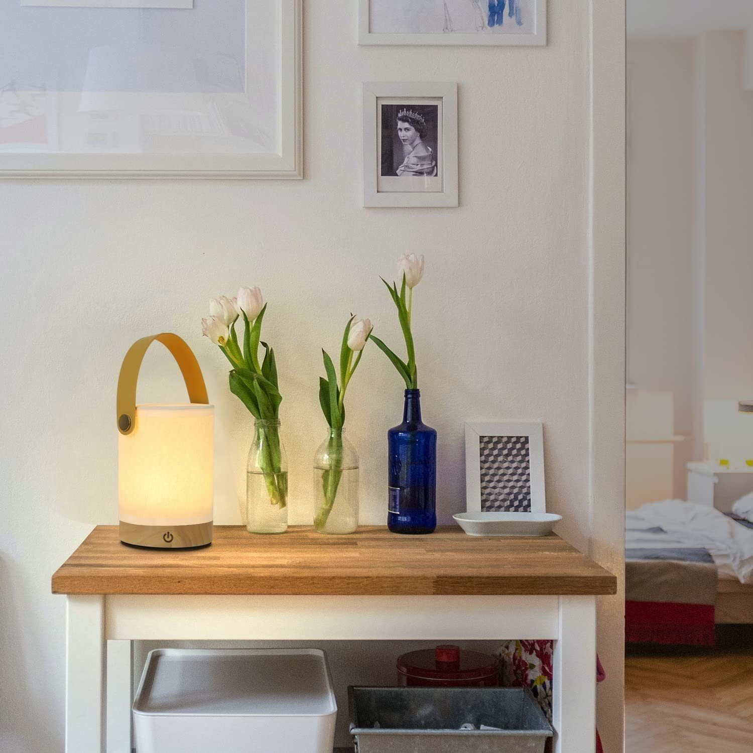 Stolik z lampą, kwiatami w wazonach i ramkami na zdjęcia.