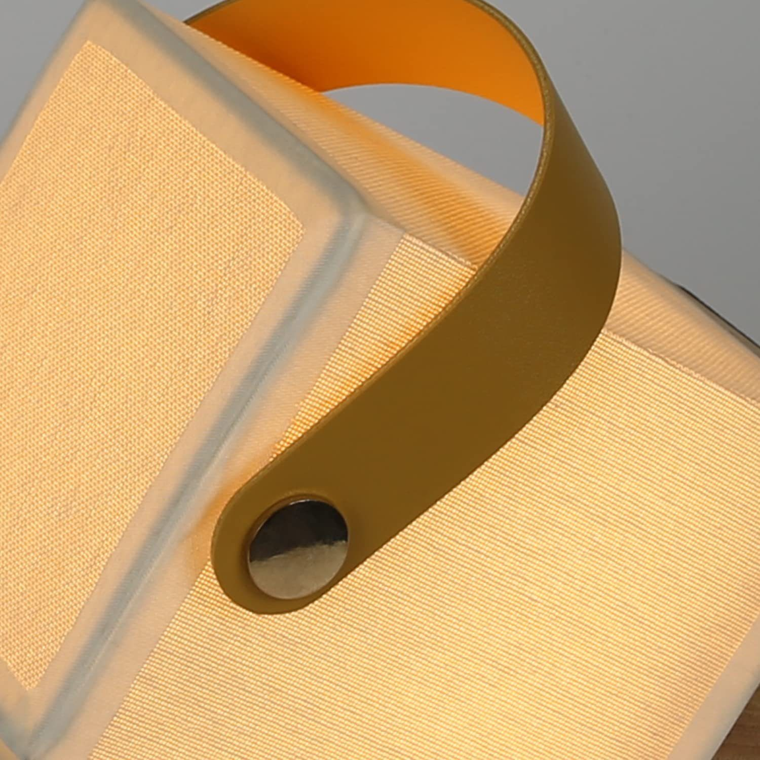 Zbliżenie lampy w kształcie kostki z żółtym uchwytem. Lampa emituje miękką poświatę.