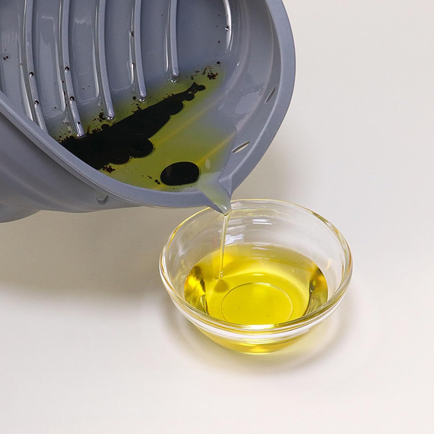 Aceite vertiéndose de un recipiente gris a un cuenco de vidrio transparente.