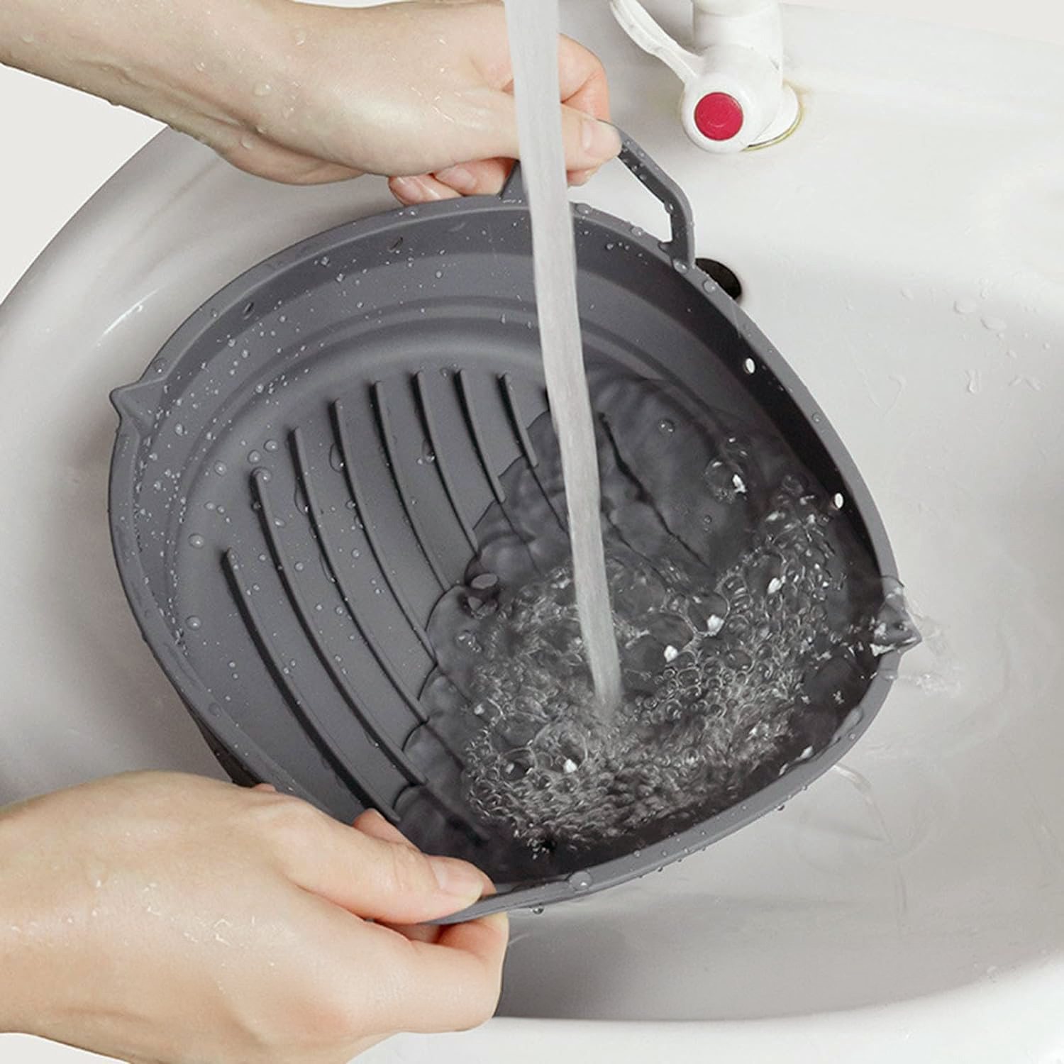Manos lavando un colador de silicona gris en un fregadero.