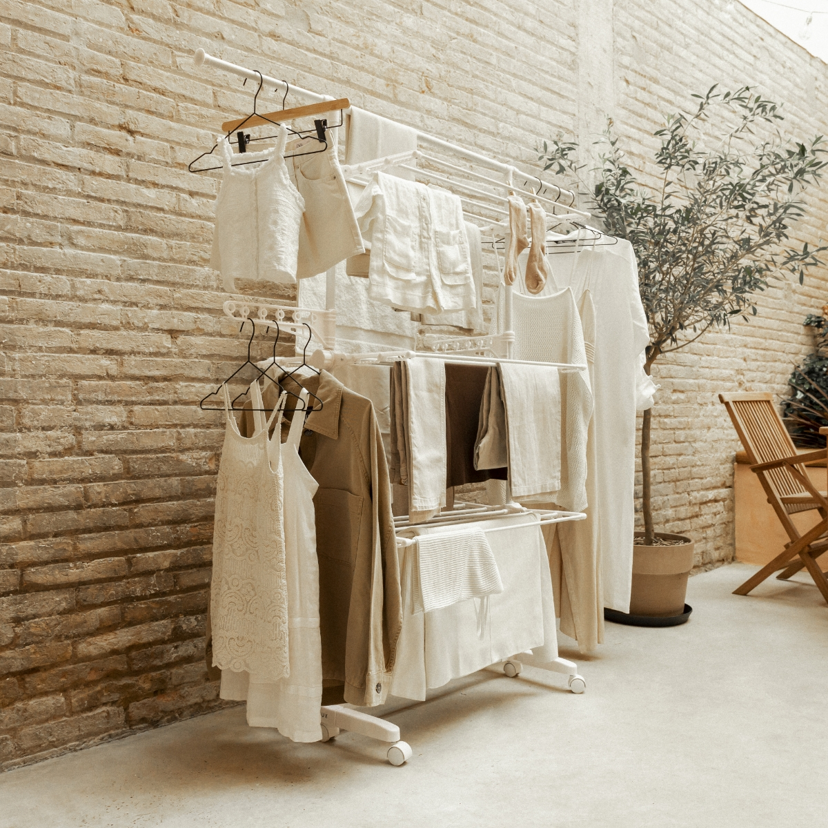 Tendedero blanco con ropa colgada. Exterior con pared de ladrillo al fondo.