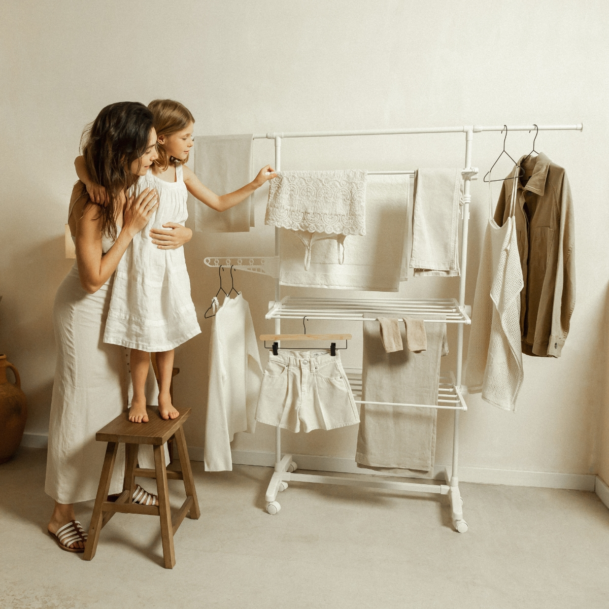 Mujer y niña junto a un perchero con ropa tendida, en una habitación luminosa con tonos neutros.