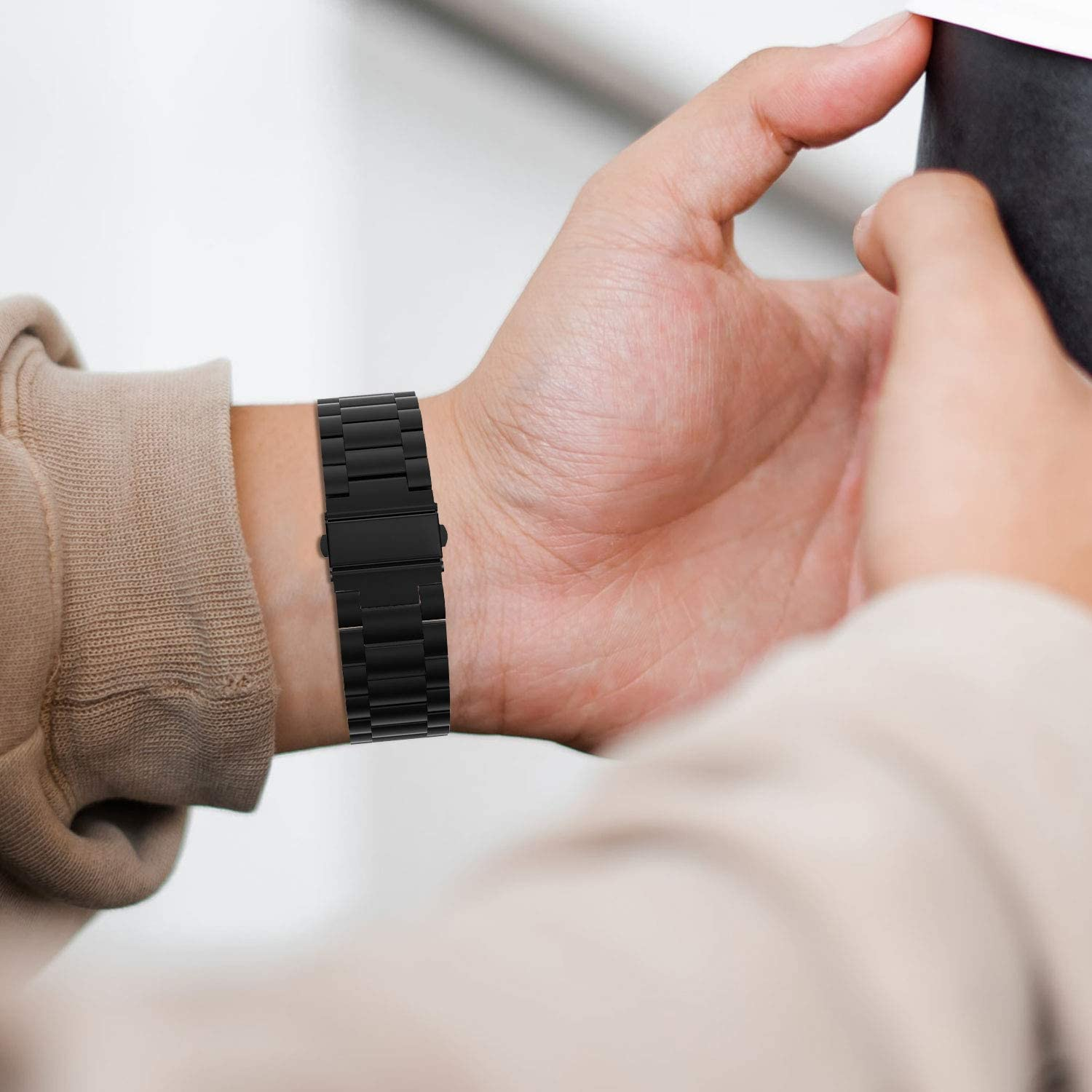 Osoba nosząca zegarek. Zegarek jest czarny i ma metalową bransoletę.