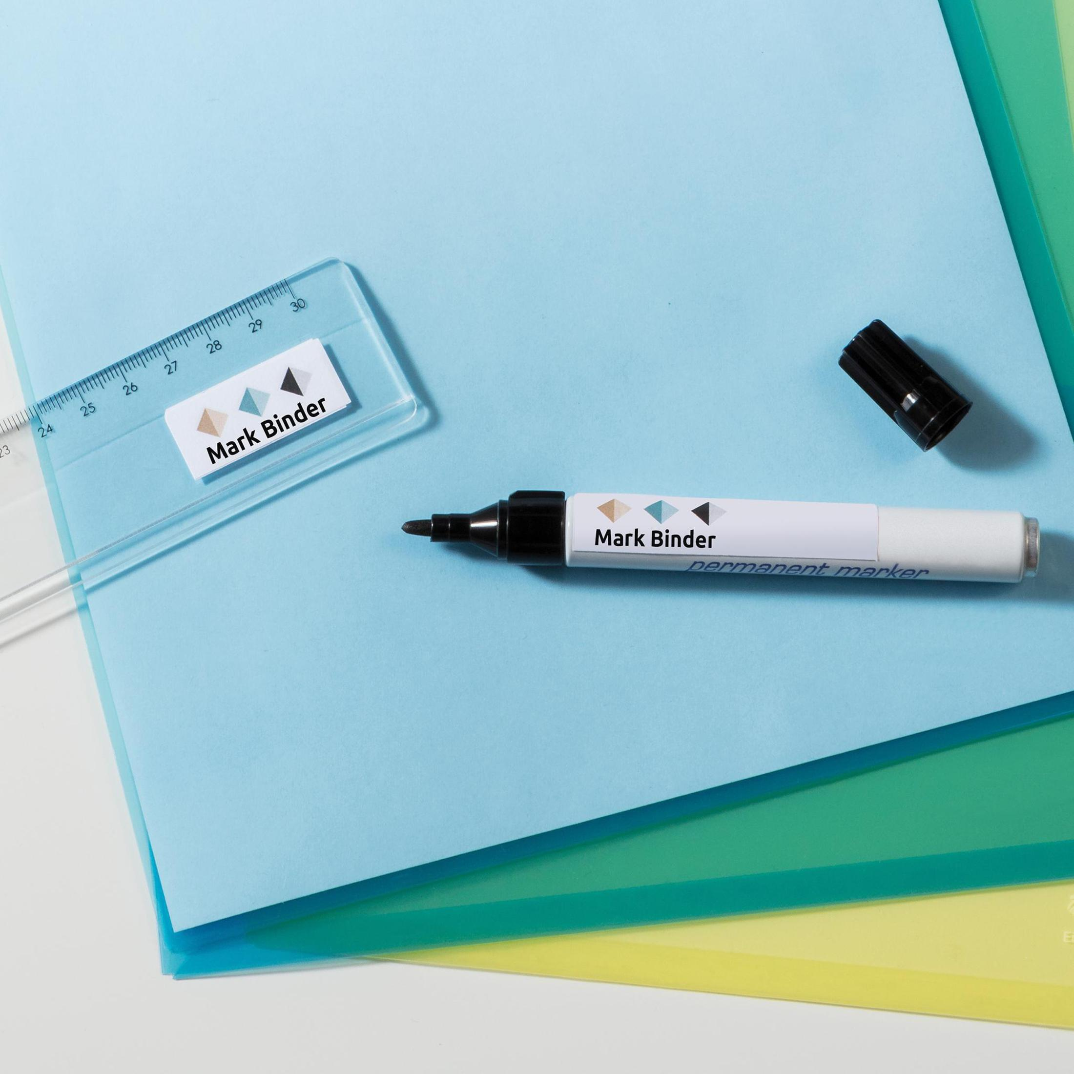 Ein Lineal und ein Permanentmarker auf blauem, grünem und gelbem Papier. Der Marker hat eine schwarze Kappe.