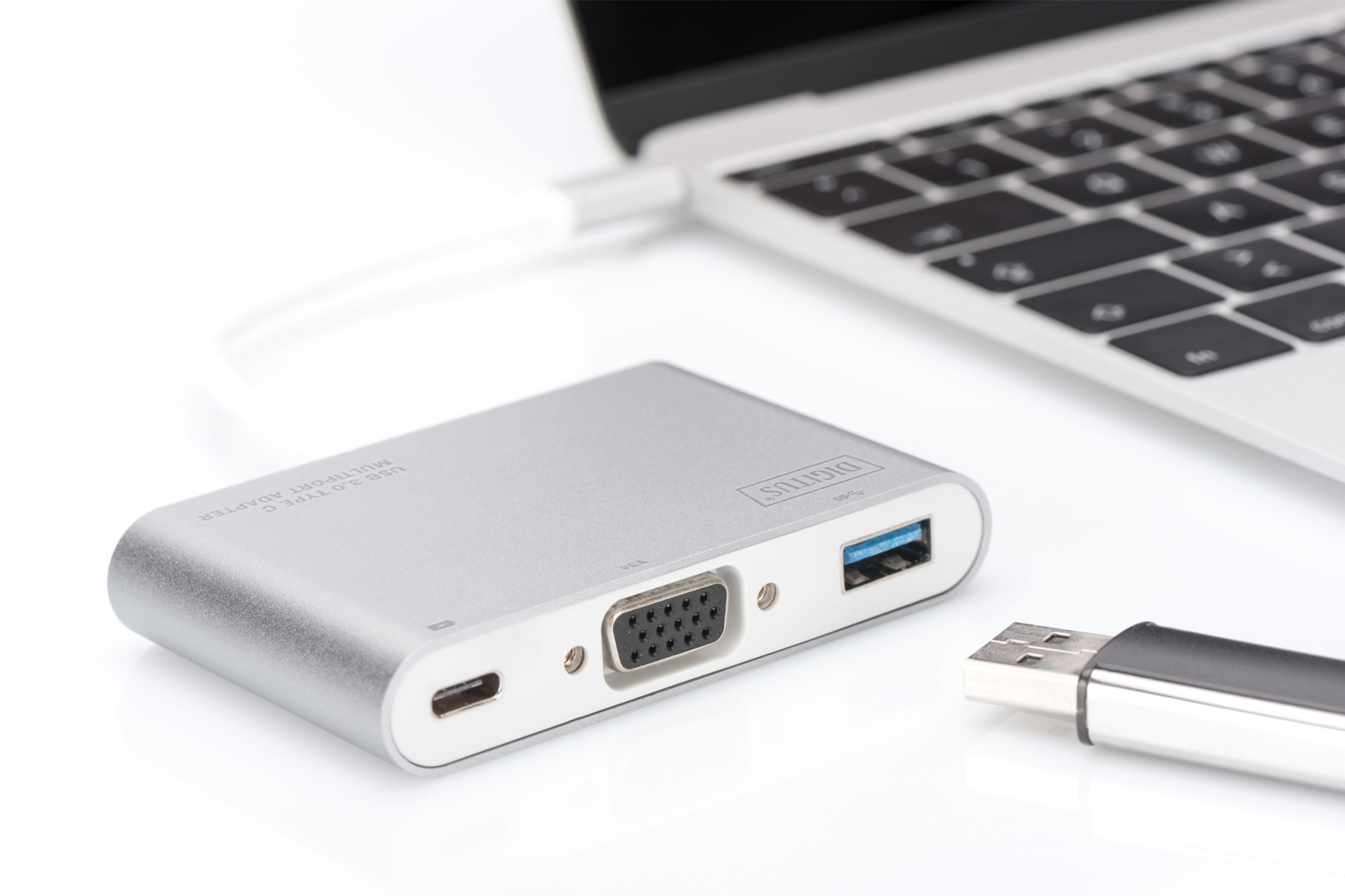 Gümüş USB-C çoklu bağlantı noktası adaptörü, dizüstü bilgisayar ve USB sürücüsü yanında.