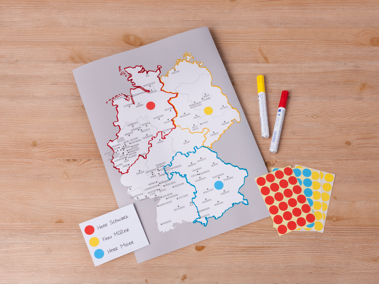 Deutschlandkarte mit farbcodierten Regionen, Markern und Aufklebern auf Holzoberfläche.